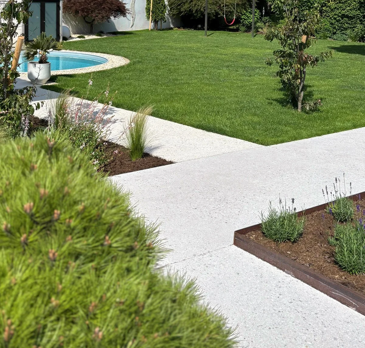 Ein gepflegter Garten mit einem Rasen, einem kleinen Pool, einem weißen Kiesweg, Büschen, Bäumen und einem Spielplatz im Hintergrund.