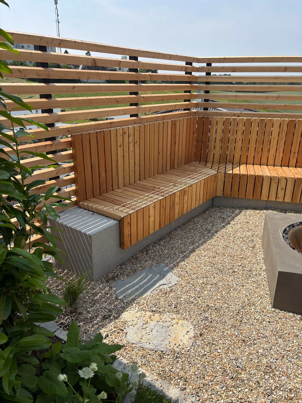 Ein Balkon mit Holzverkleidung und einer kleinen Sitzbank, umgeben von einer Holzwand und einem Kiesboden.