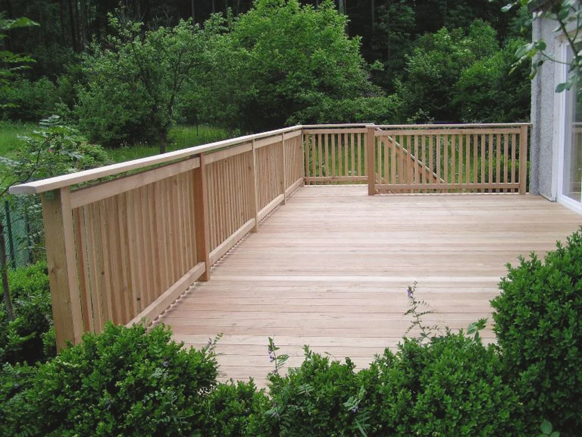 Holzterrasse mit Holzgeländer in einem grünen Garten.