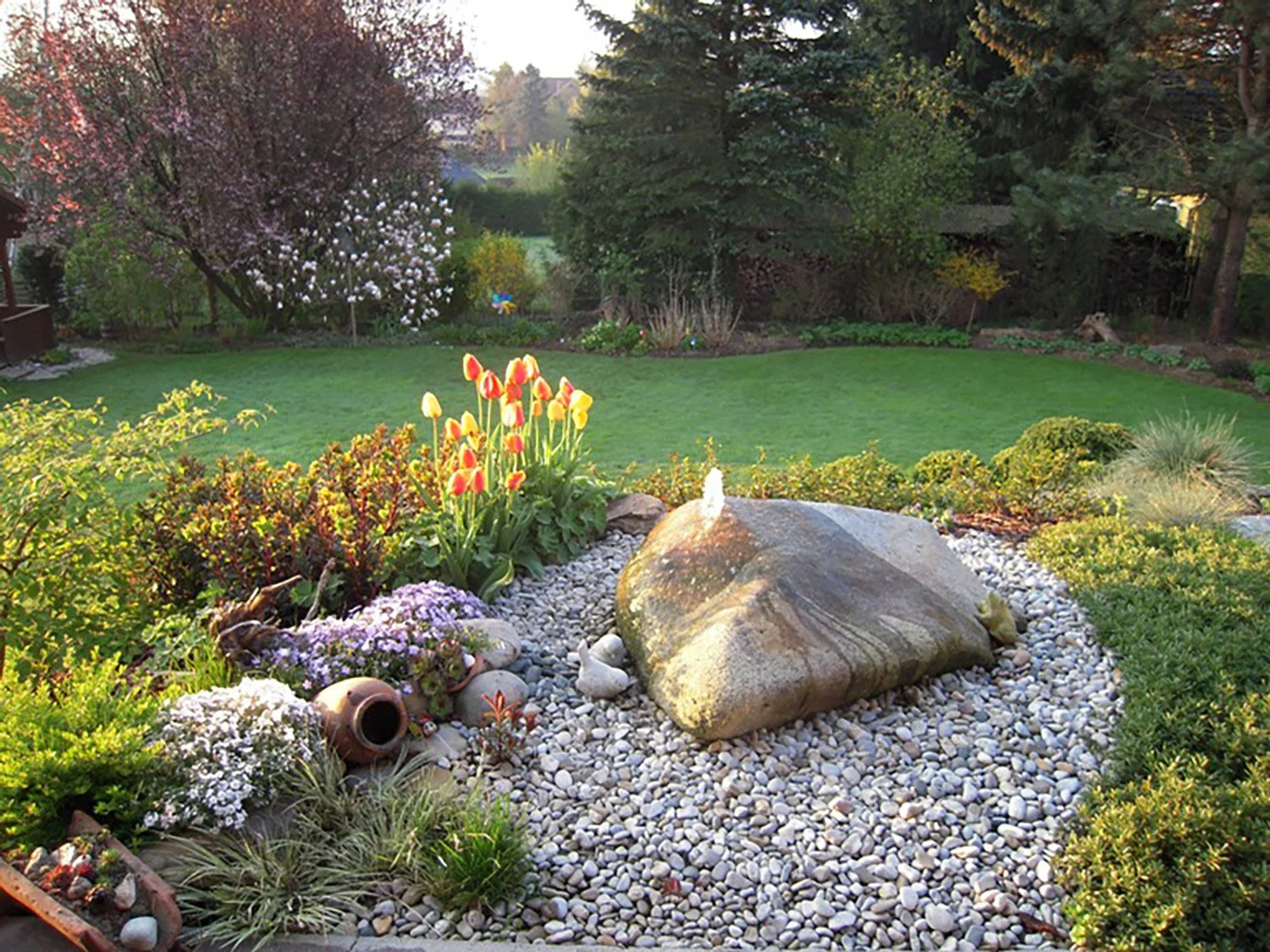 Garten mit Rasen, bunten Blumen, großen Steinen und Dekorationen. Gartengestaltung Österreich