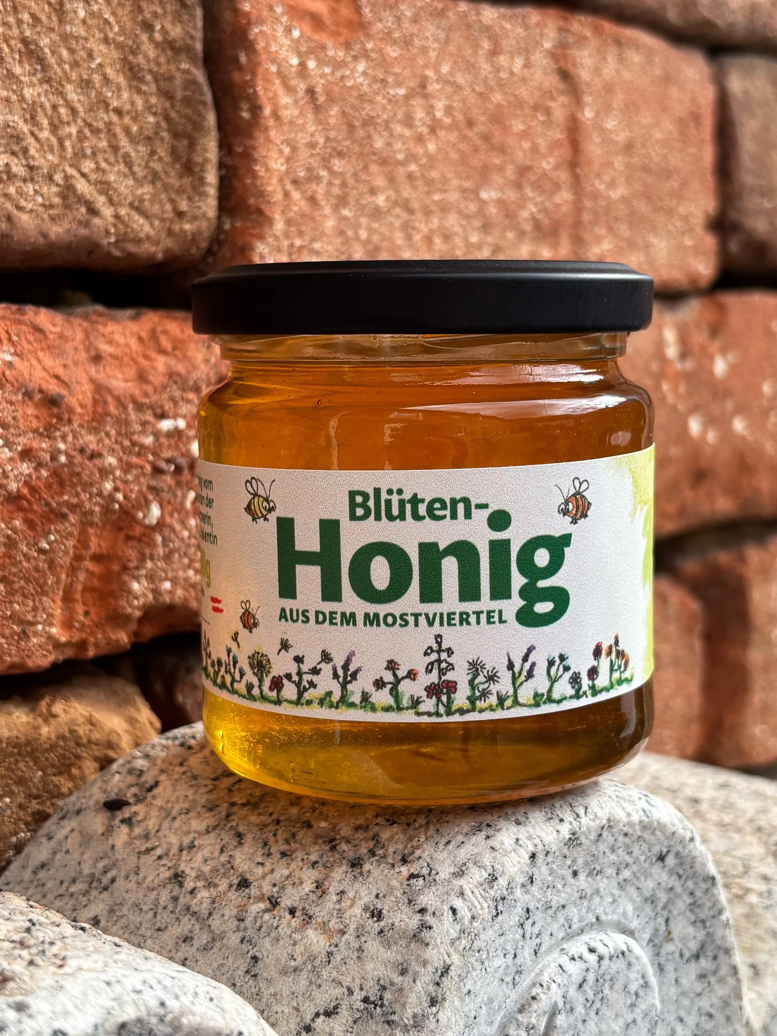 Ein Glas mit Honig, das auf einem Stein liegt, vor einem Backsteinmauer im Hintergrund.