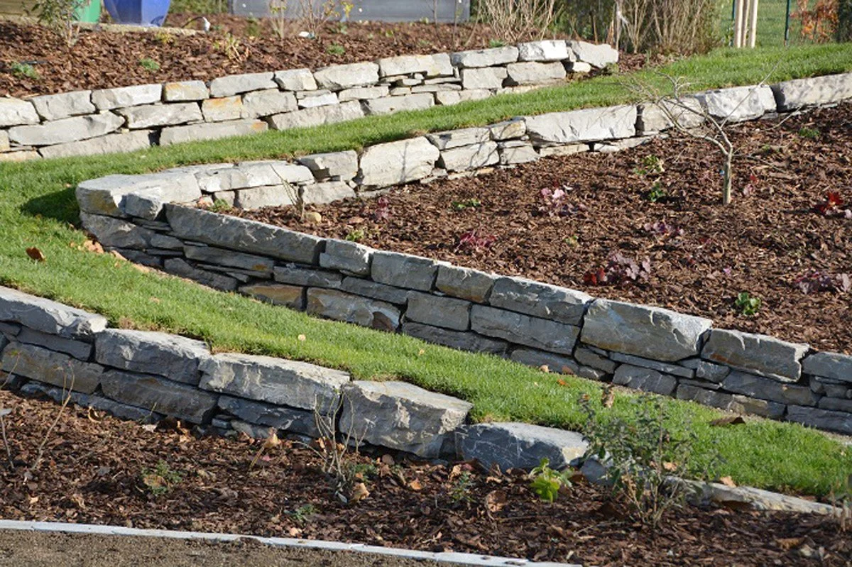 Steinmauer mit Terrassen, die mit Grass bedeckt sind, und einem Garten mit kleinen Pflanzen.