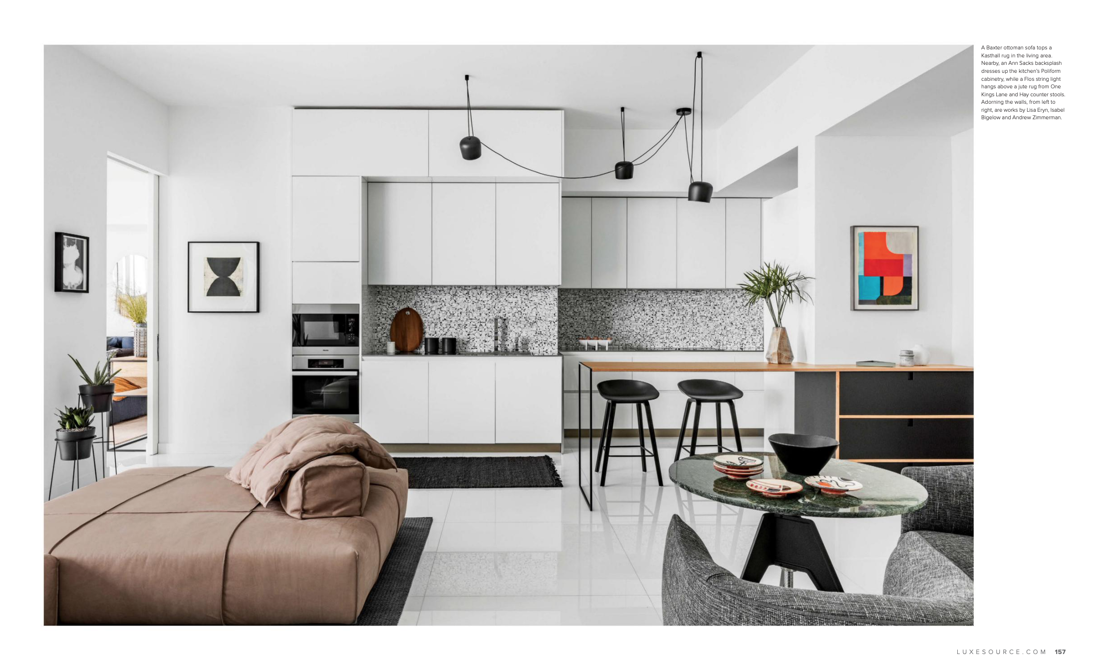 Modern open-concept living space with a kitchen, dining area, and sitting area. The kitchen features white cabinets, black pendant lights, black and white terrazzo backsplash, and a breakfast bar with black barstools. The dining area has a round tabl