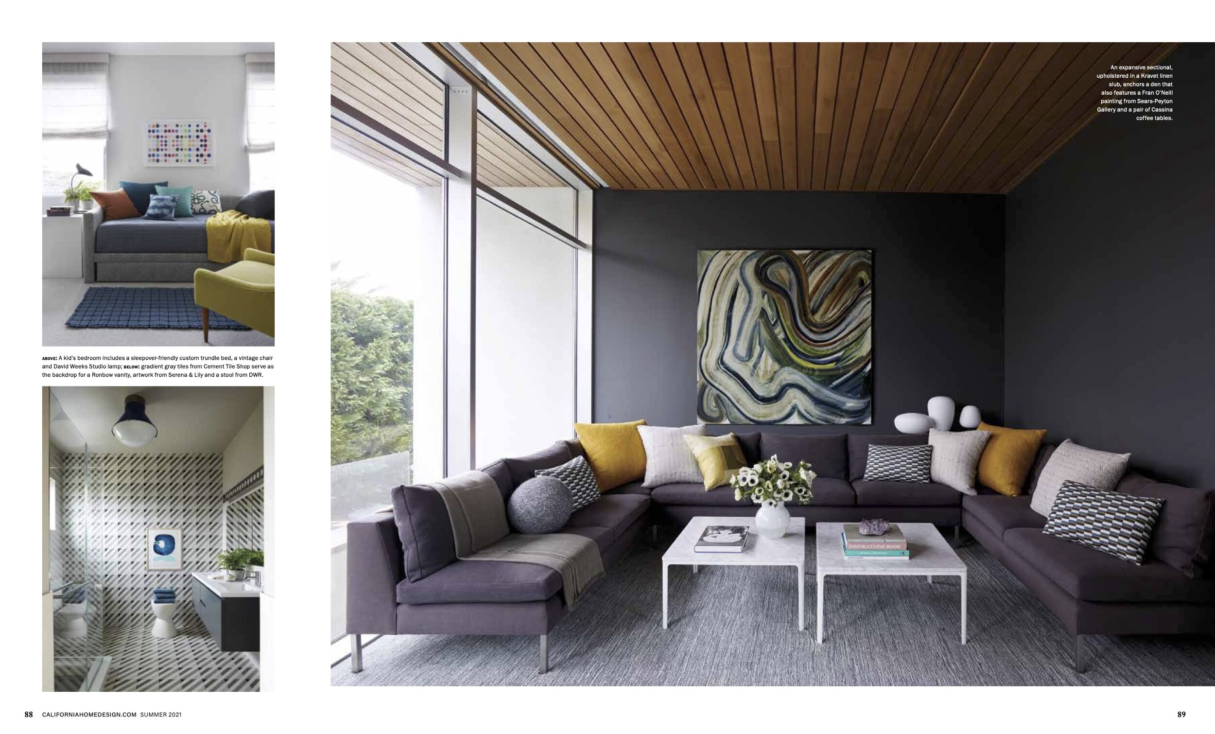 Living room with a sectional sofa, abstract artwork on a dark wall, large windows with wooden ceiling above, pillows on the sofa, a white coffee table with books and a vase, and modern decorative objects.