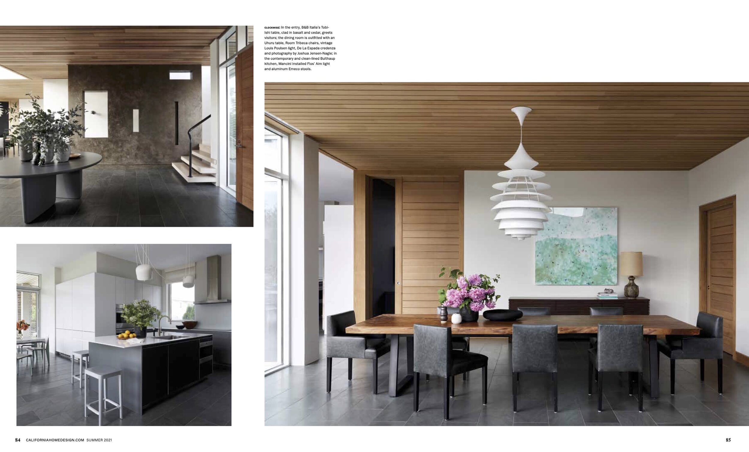 Interior view of a modern home featuring a dining area with a wooden table, black chairs, and a sculptural white pendant light. The space has a wooden ceiling and sliding door, with contemporary art on the wall and a sideboard with a lamp. Adjacent a