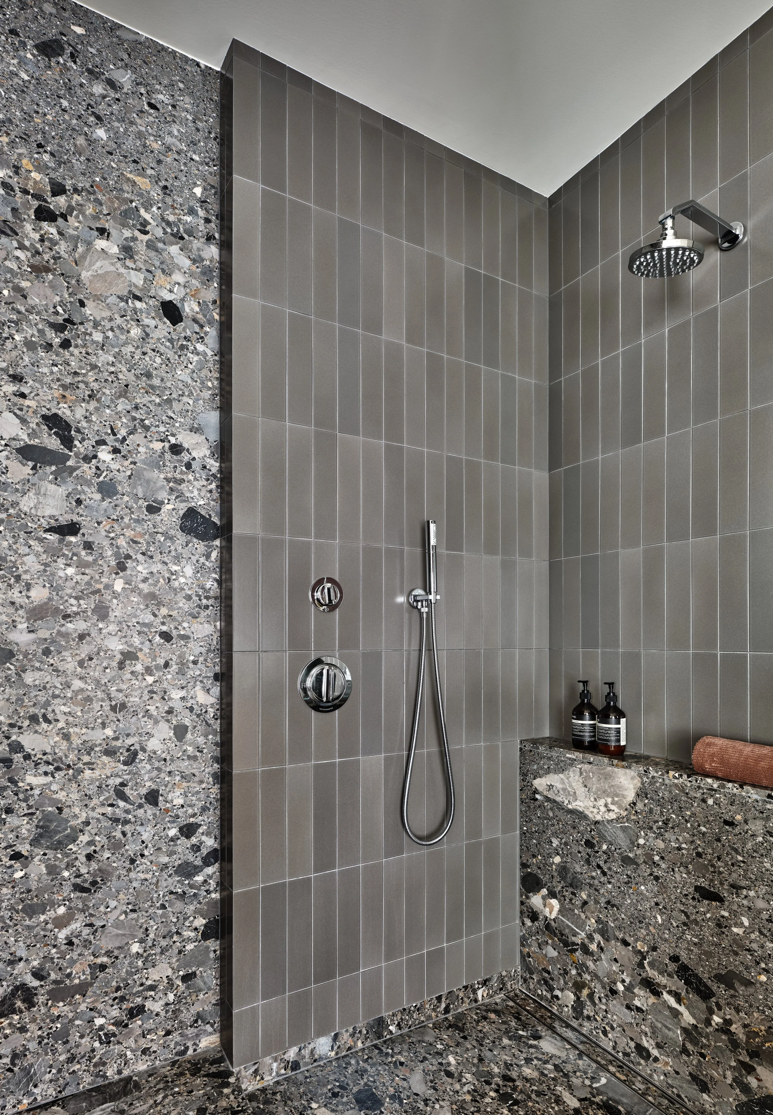 Modern walk-in shower with gray tiles, a rain showerhead, handheld shower, and marble accents.