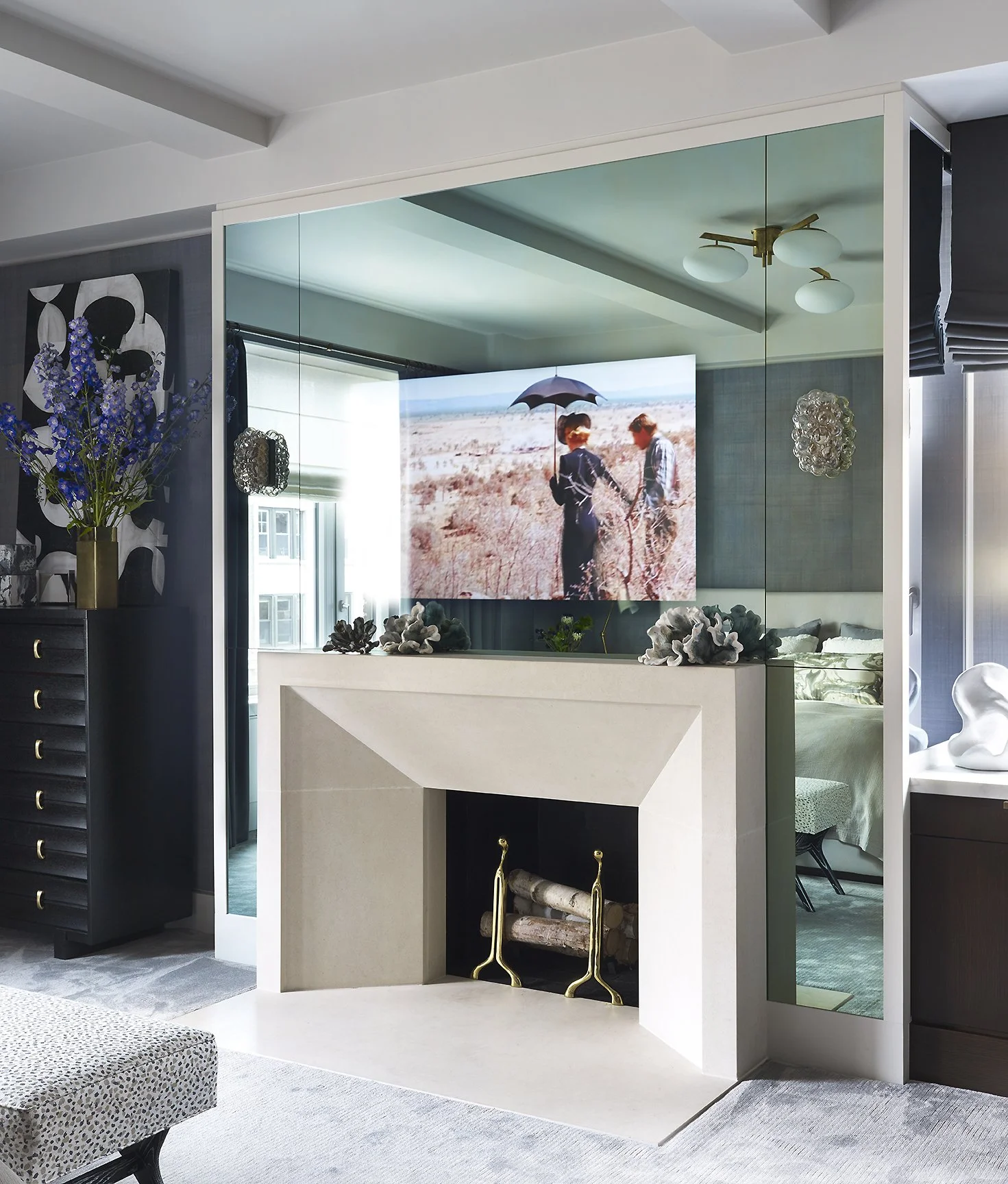Living room with a fireplace, flat-screen TV displaying people with an umbrella, and decorative plants.
