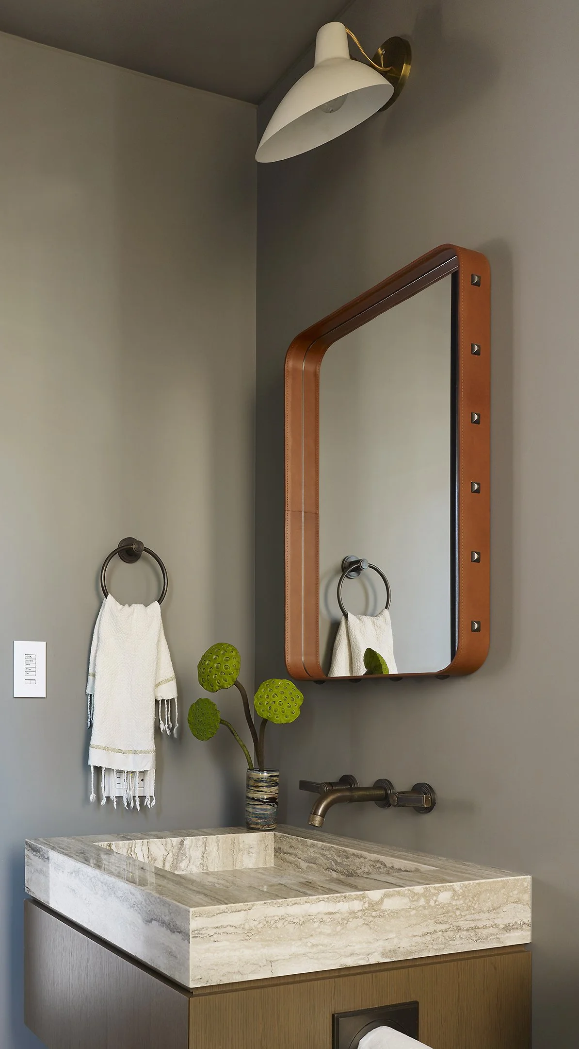 Bathroom vanity with a marble sink, a decorative plant, a wall-mounted mirror with a wooden frame, a wall sconce light, and a towel hanging on a towel ring.