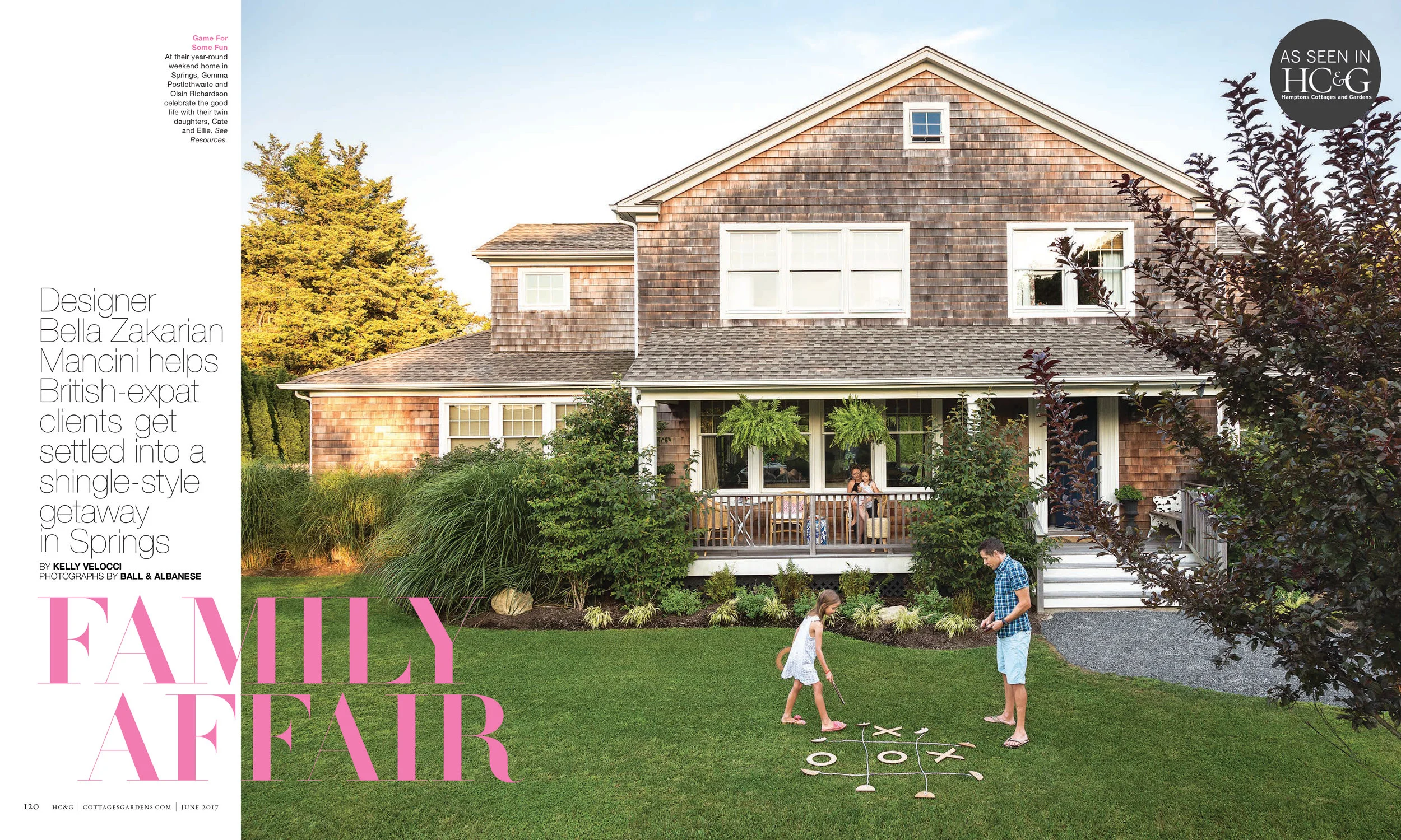 A family playing hopscotch on the front lawn of a brown, shingled house with a porch and lush greenery.