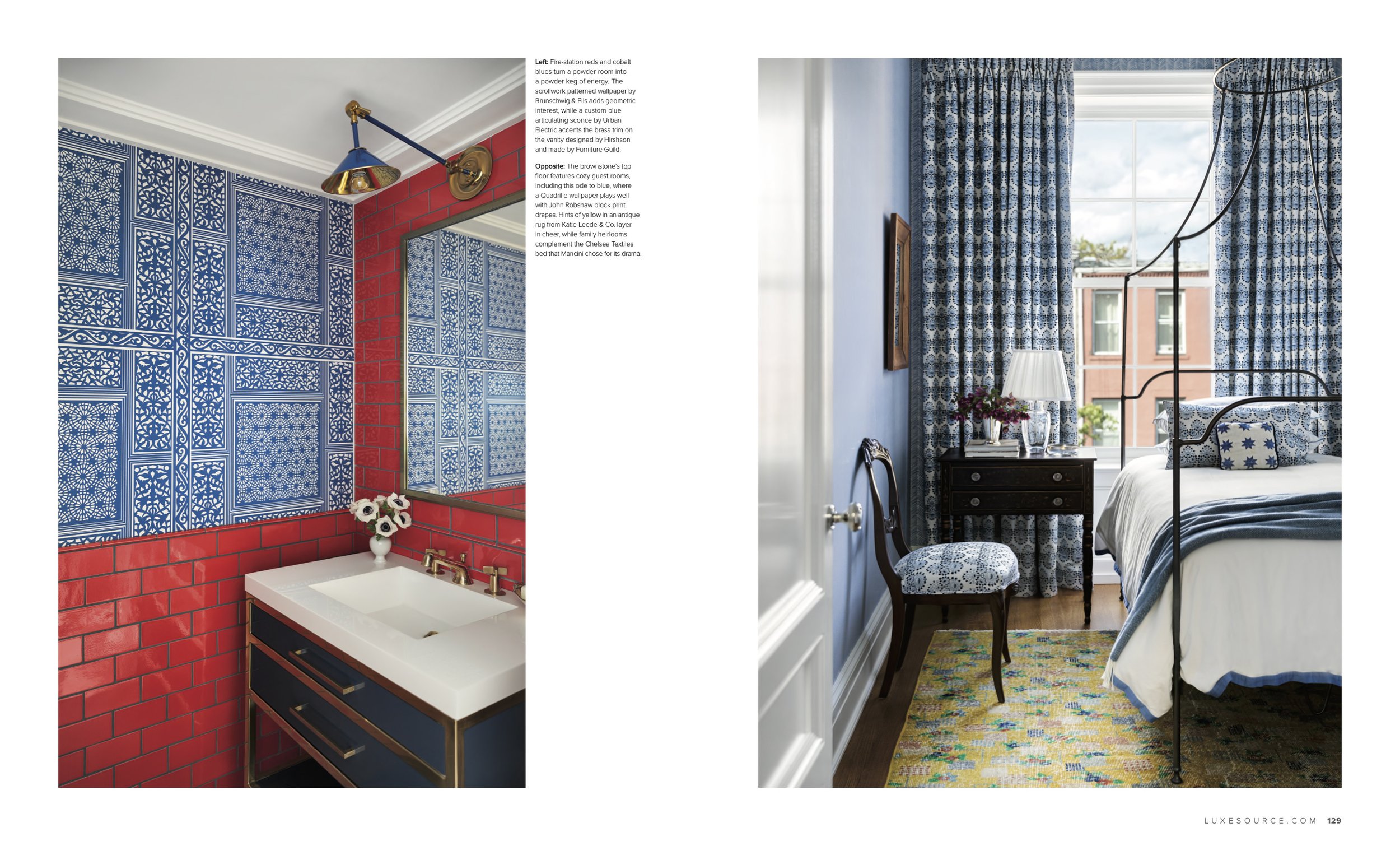 A bedroom with a black metal bed frame, blue and white patterned curtains, a dark wood nightstand with a white lamp and flowers, a patterned rug, and a large window showing buildings outside.