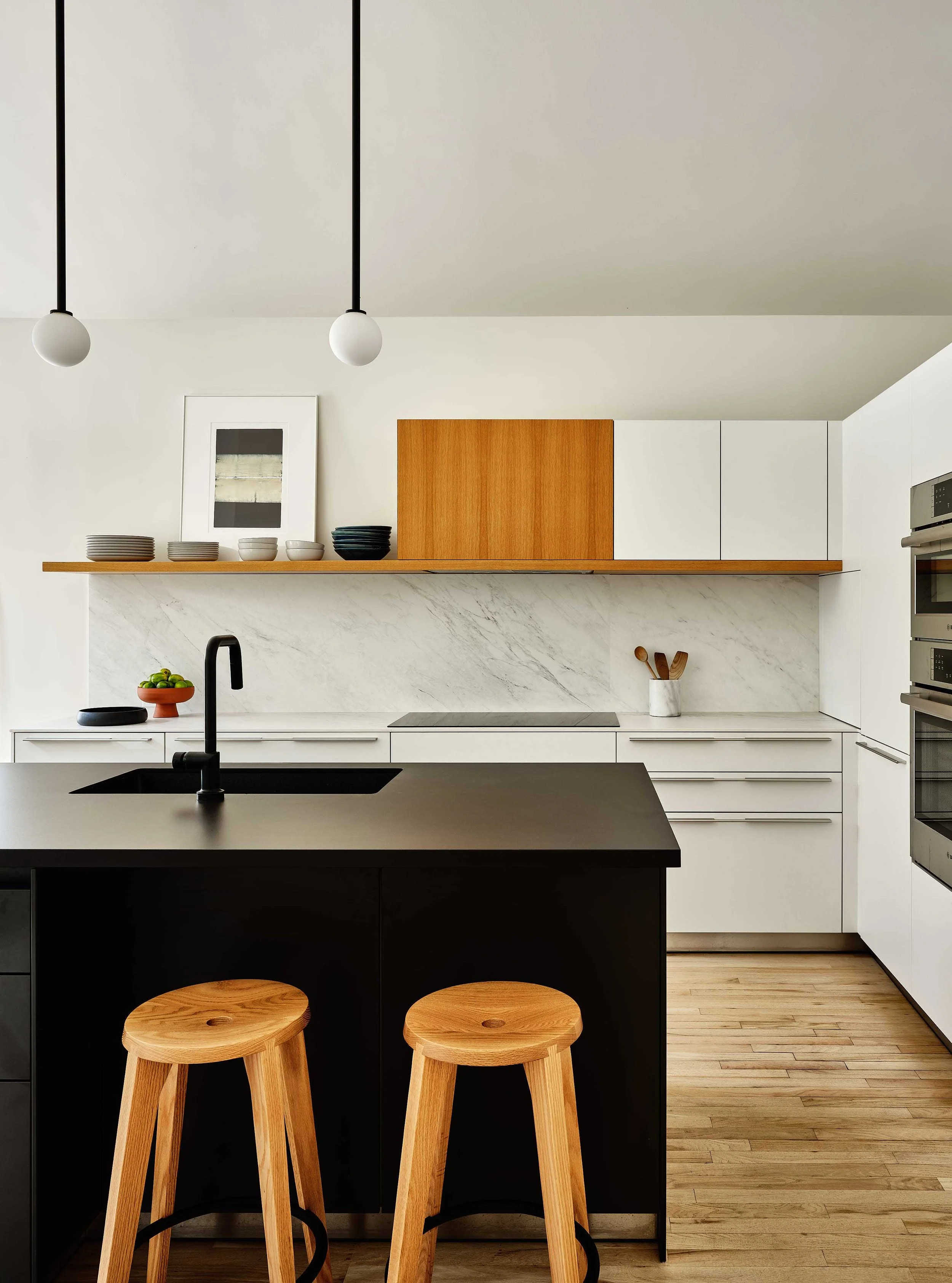 Modern kitchen with white upper cabinets, black island with bar stools, open wooden shelf, and marble backsplash.
