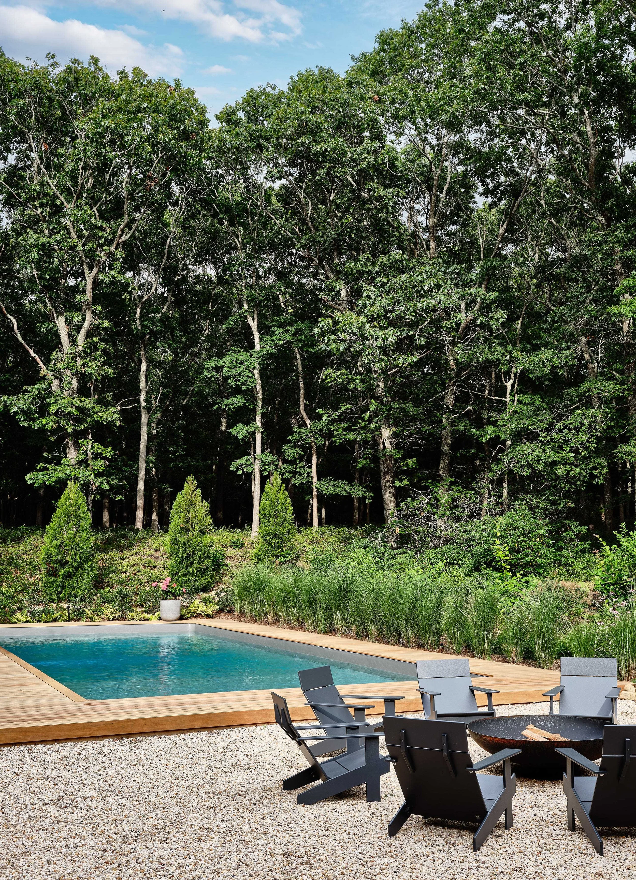 Backyard with a swimming pool, surrounded by trees, outdoor chairs, and a fire pit.