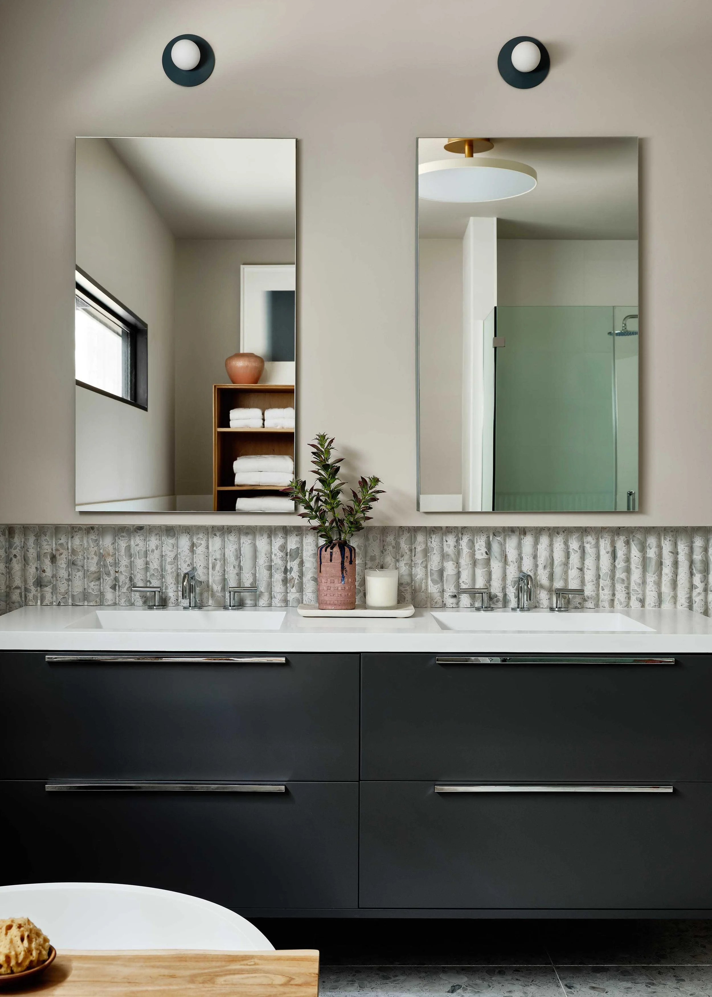 Modern bathroom with dual sinks, large mirrors, potted plant, candles, and beige walls.