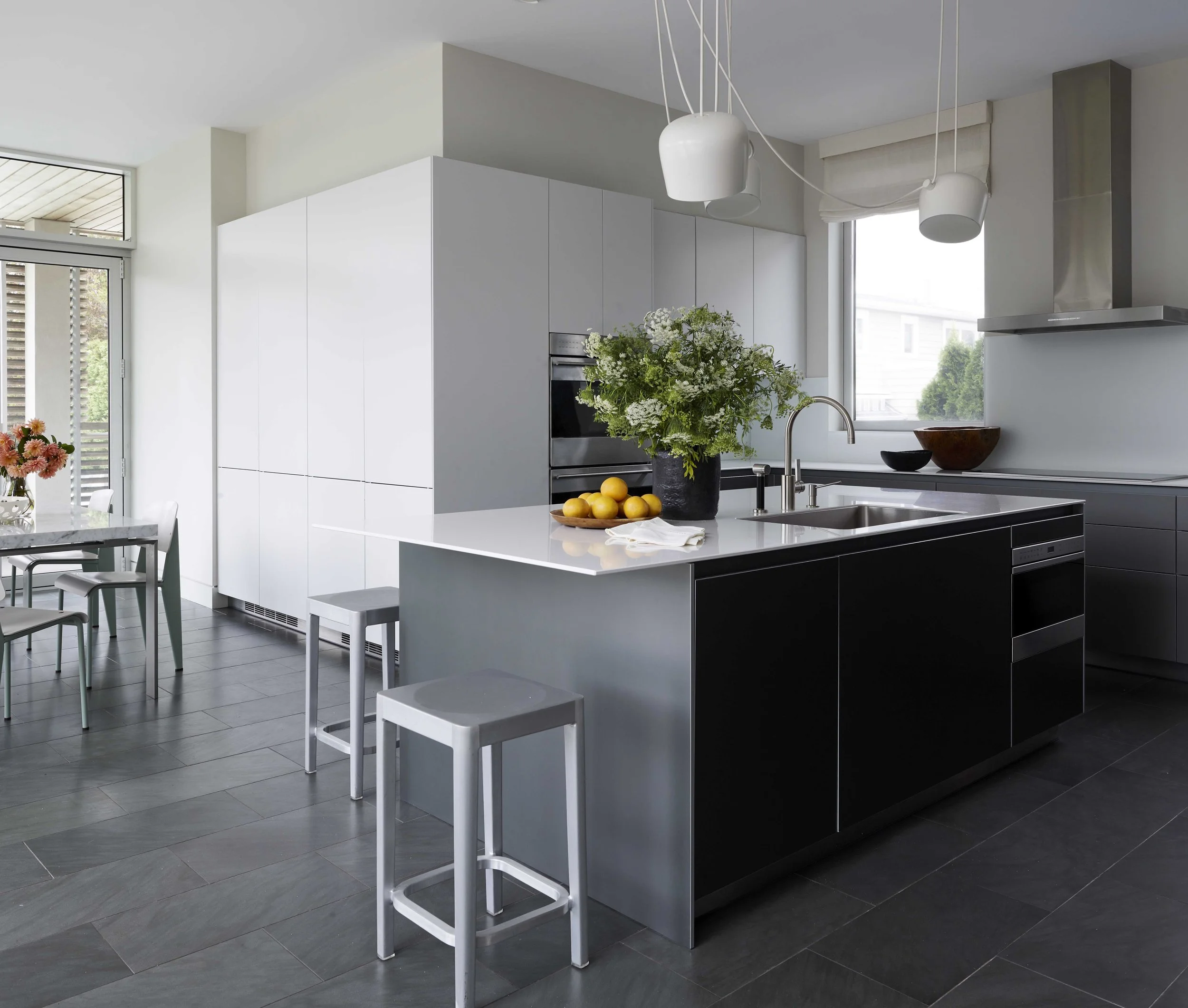Modern kitchen with black and white cabinetry, a kitchen island with a sink, a vase of green and white flowers, lemons, and hanging pendant lights.