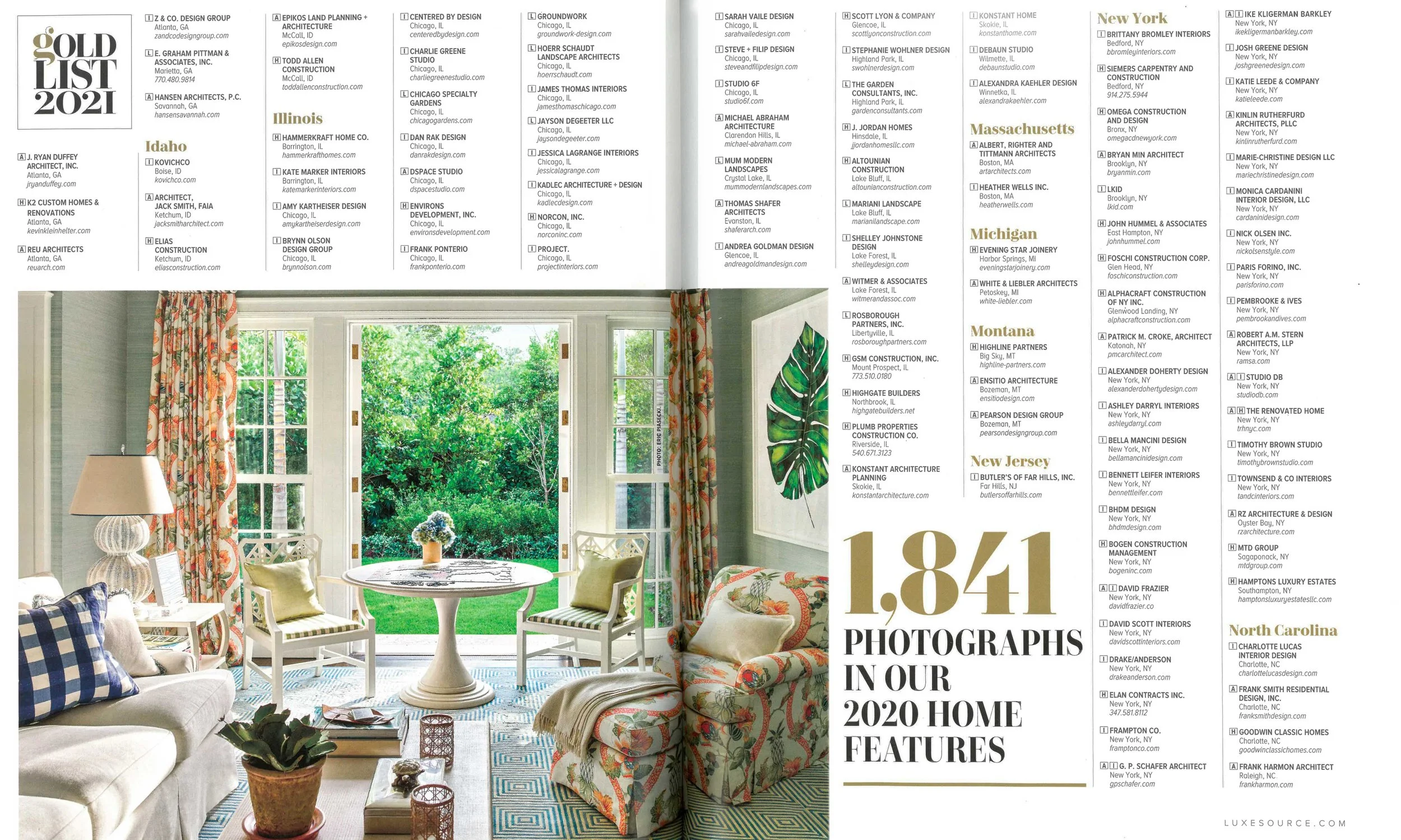 Bright living room with large windows showing greenery outside, decorated with floral curtains, patterned sofa, armchairs with pillows, a round table, and a framed botanical print on the wall.