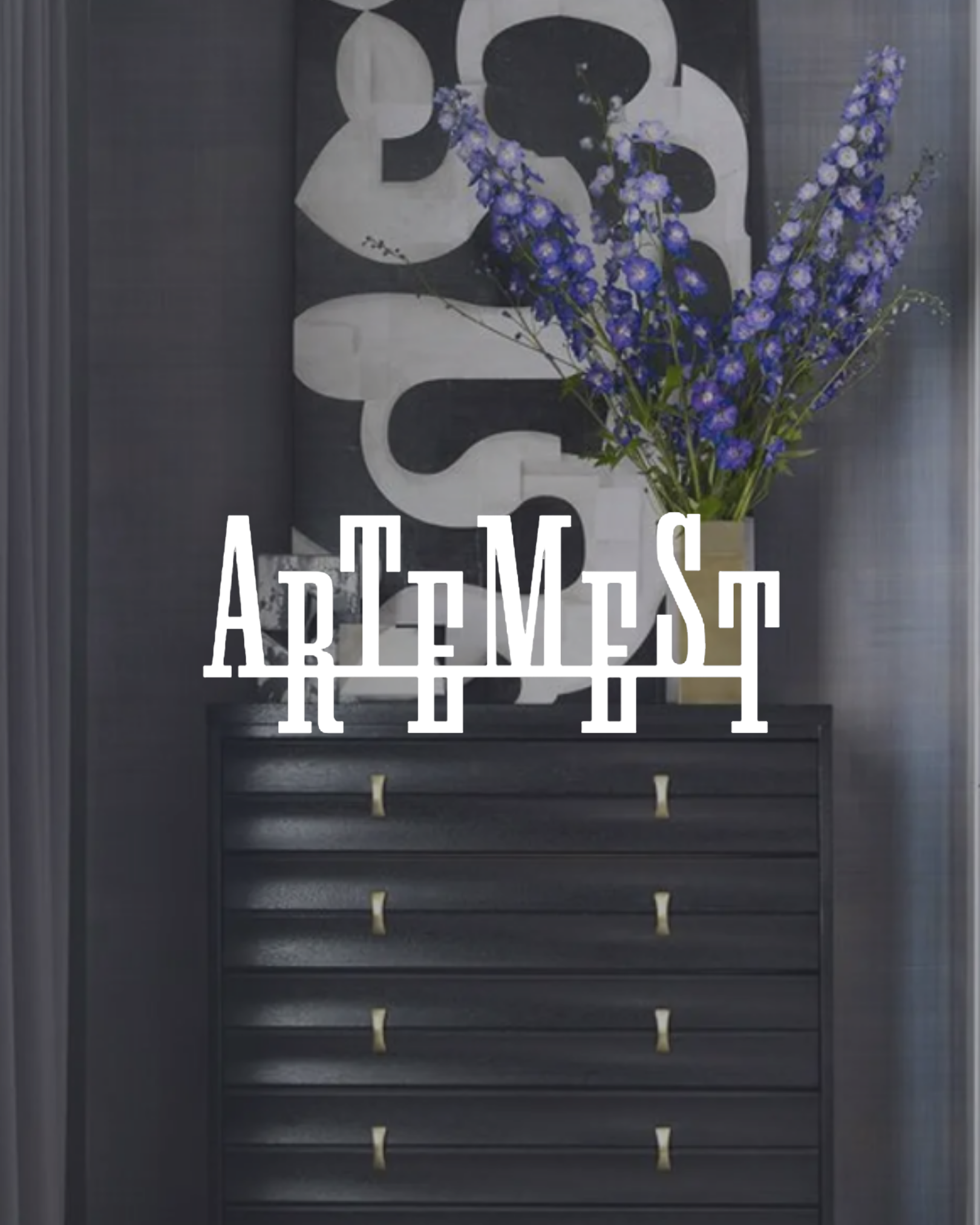 A black dresser with drawers and gold handles, behind which is a large abstract black and white artwork, with a vase of purple flowers on top and the word ARTEMEST written in white text in front.