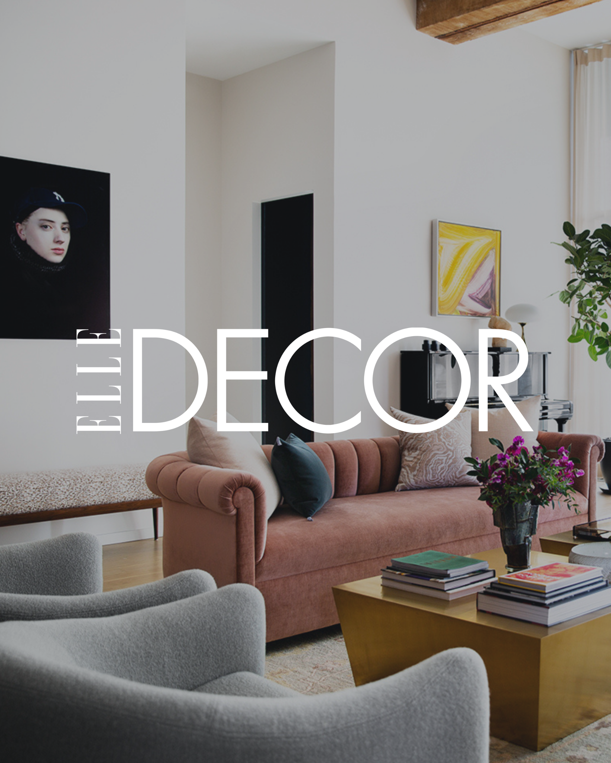 Modern living room with pink velvet sofa, gray armchair, coffee table with books, colorful artwork, potted plant, and framed photographs on the wall.