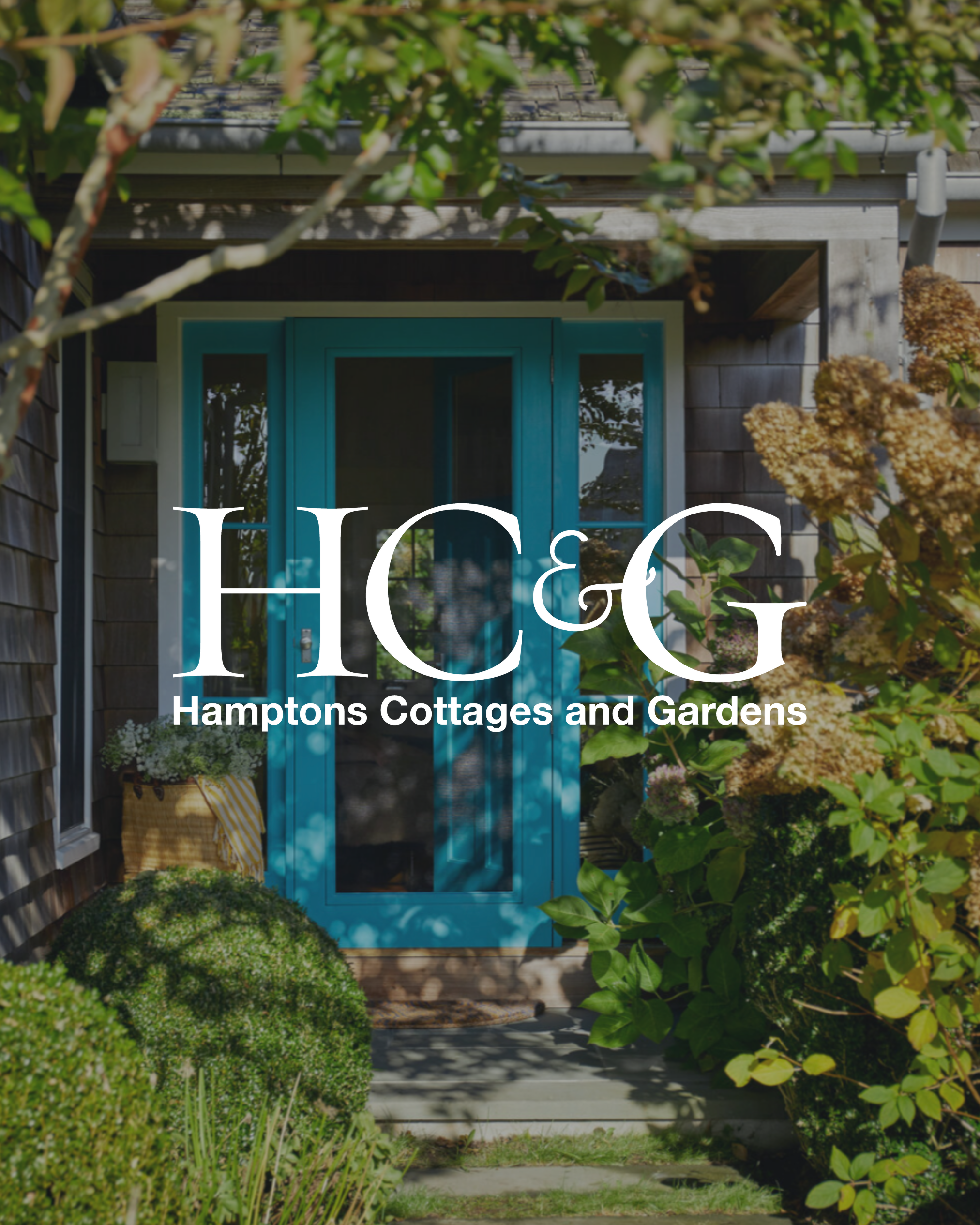 Front entrance of a cottage with a bright teal door, surrounded by lush green plants and shrubs, with the logo 'HC&G Hamptons Cottages and Gardens' overlayed.