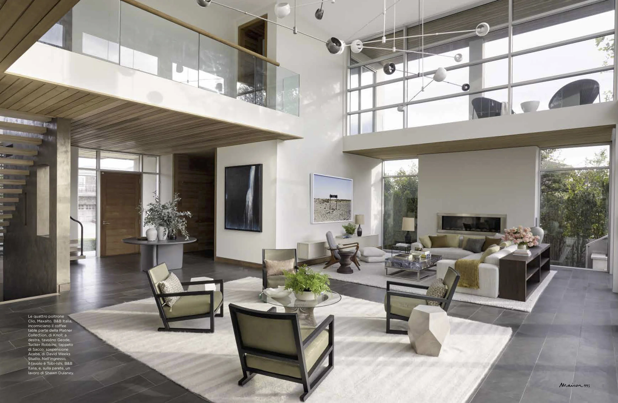 Open-concept living room with modern furniture, large windows, wood accents, and a loft area.