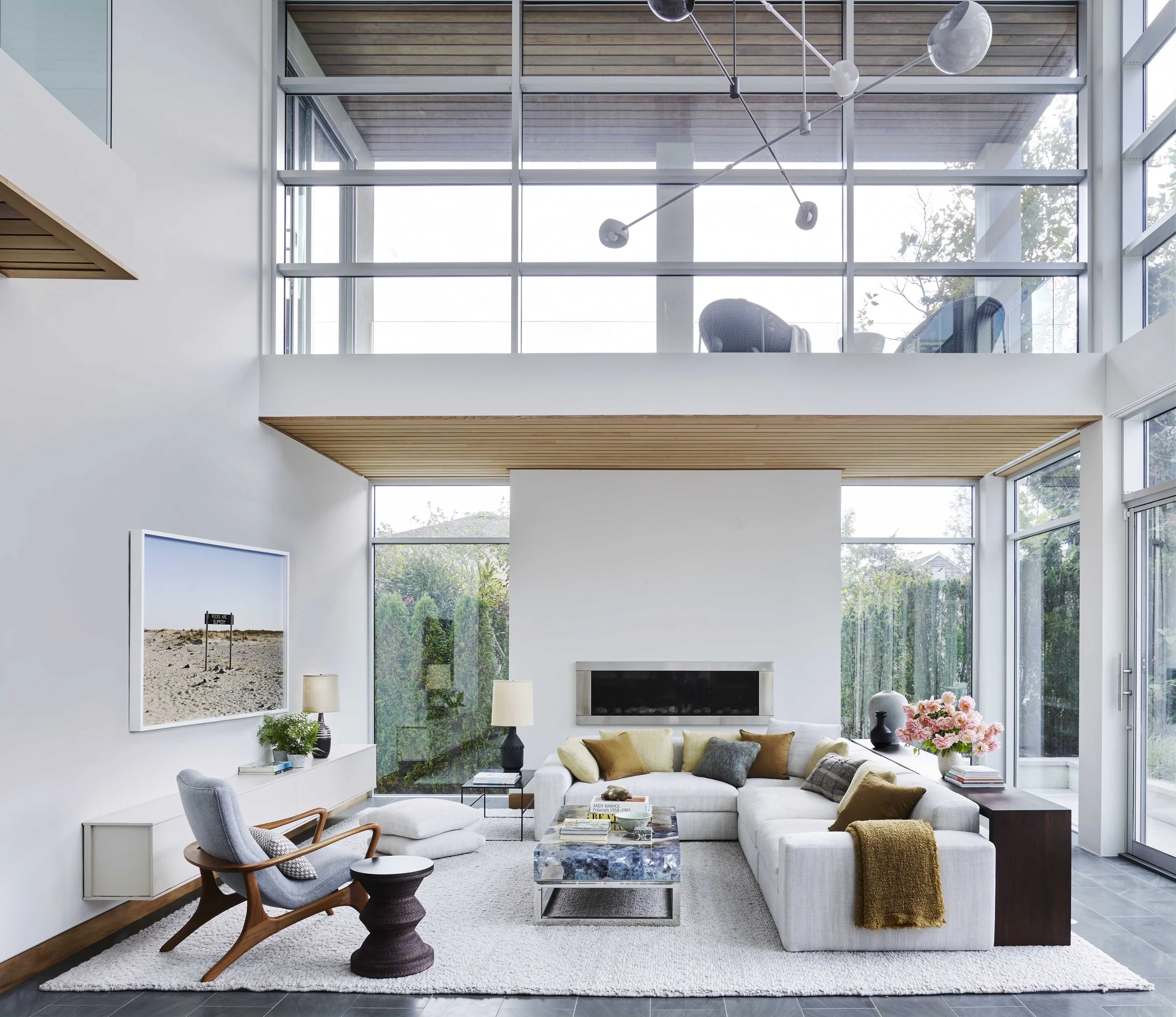 Modern living room with a white sectional sofa, armchair, coffee table, and large windows in a high-ceiling home
