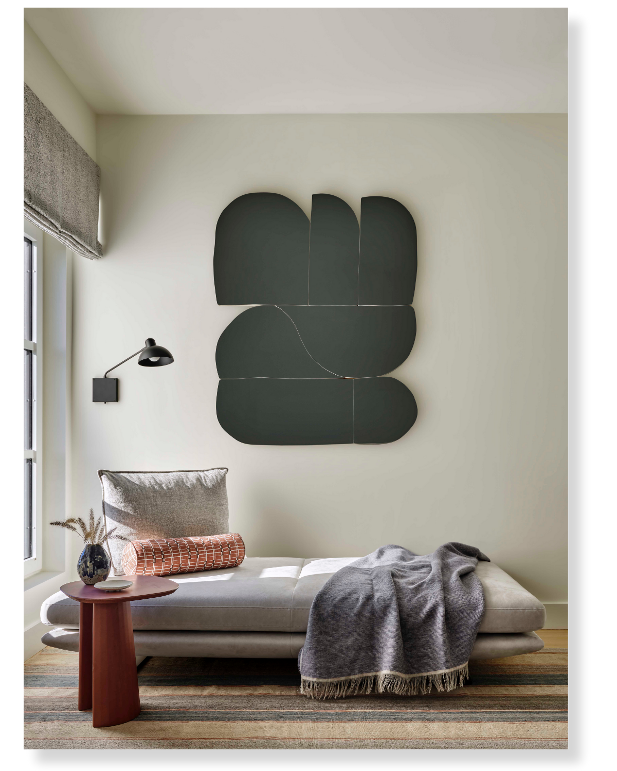 Modern living room with a gray chaise lounge, black wall art, a side table with a vase, and a gray blanket.