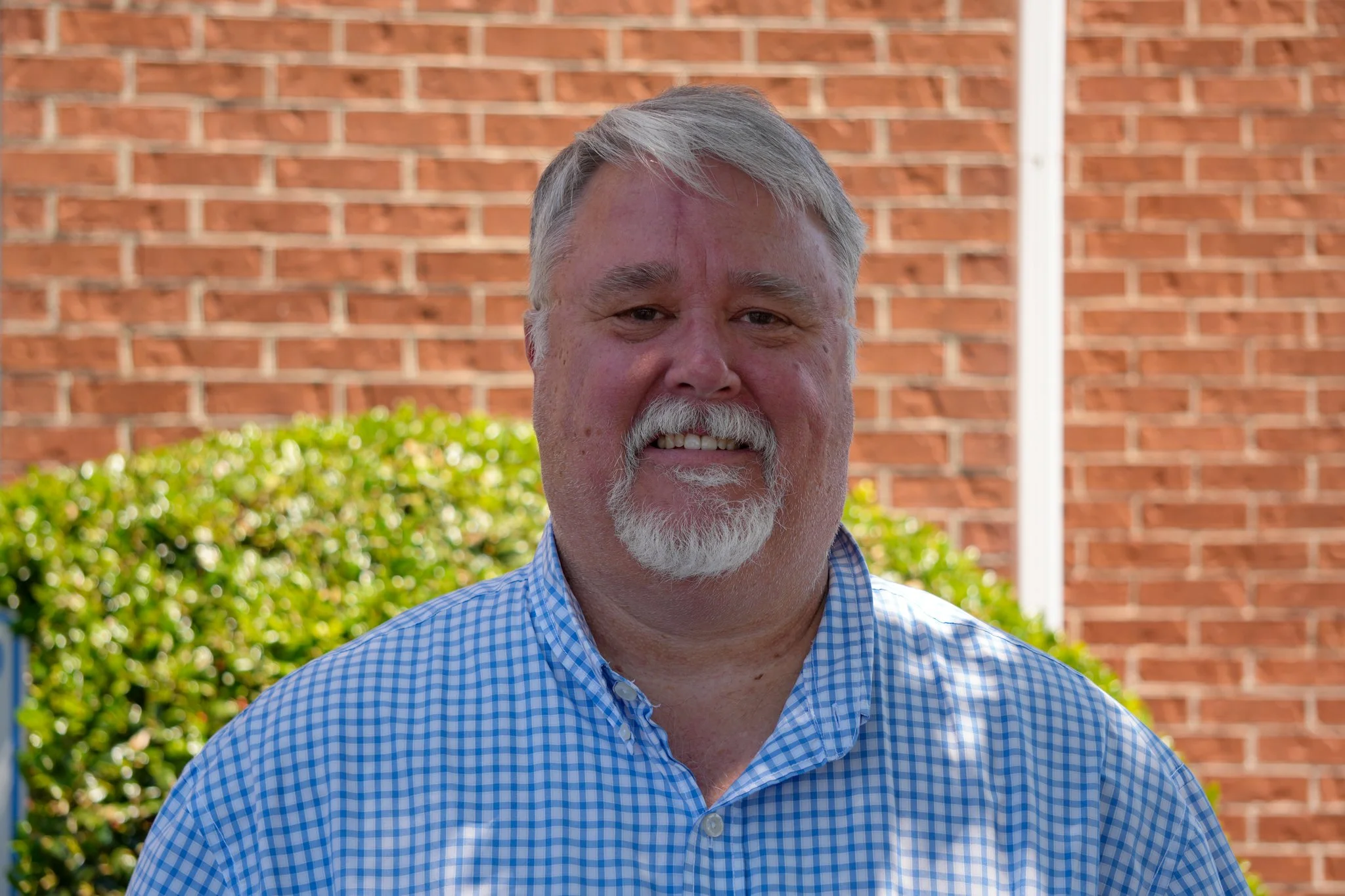 A middle-aged man with glasses, gray hair, and a goatee, wearing a blue shirt and dark blazer, smiling for a photo against a plain white background.