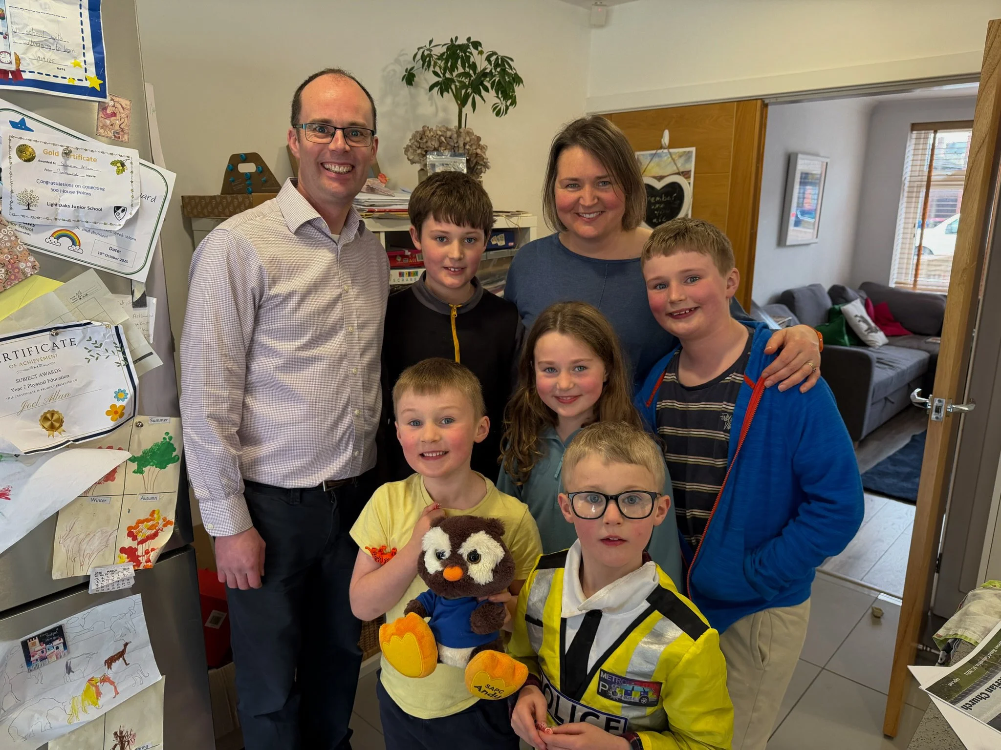 A group of seven people, including four children and three adults, smiling and posing outdoors in a garden.