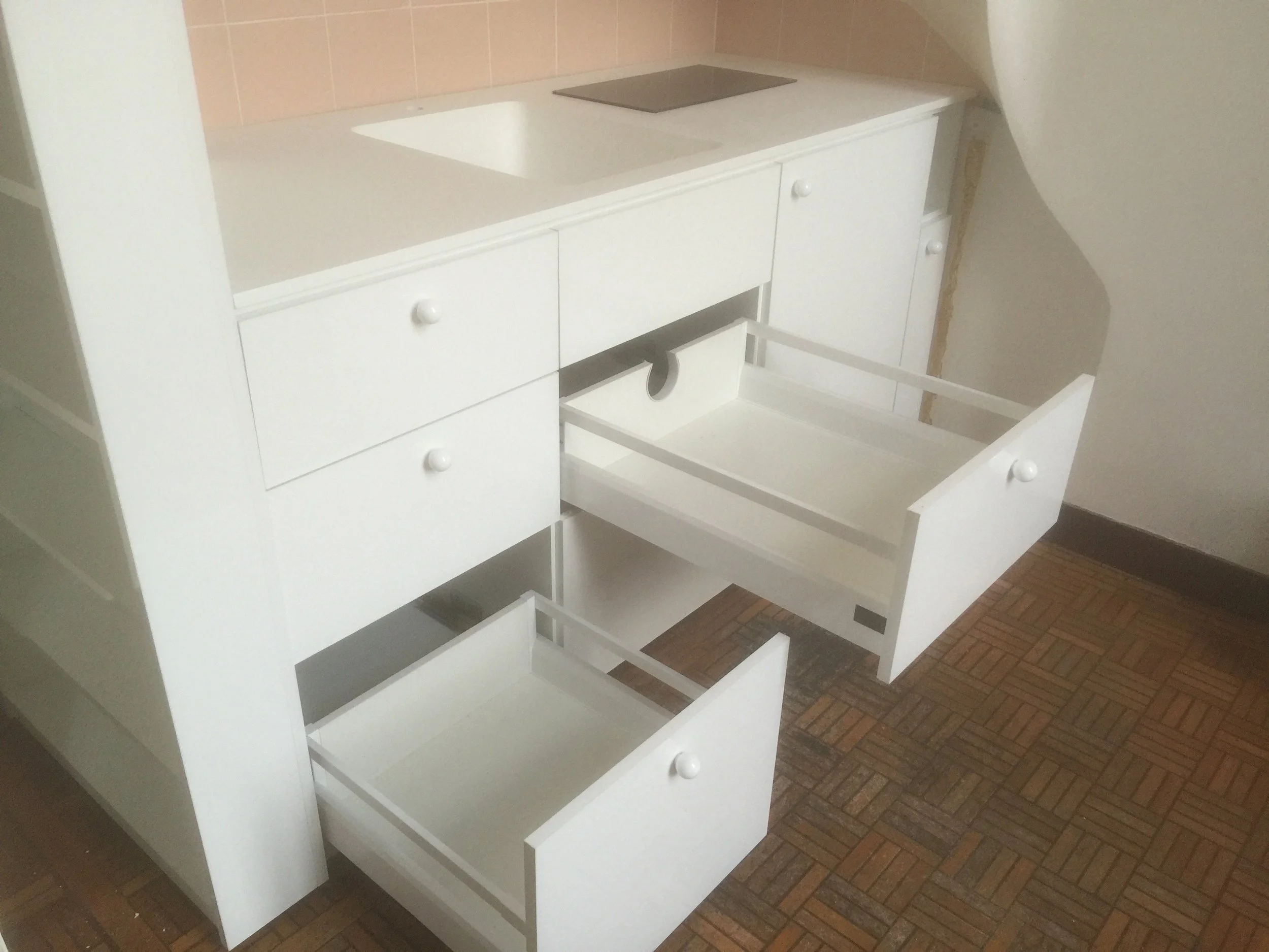 White wooden cabinet with open drawers and cupboard doors, placed on a wooden parquet floor.
