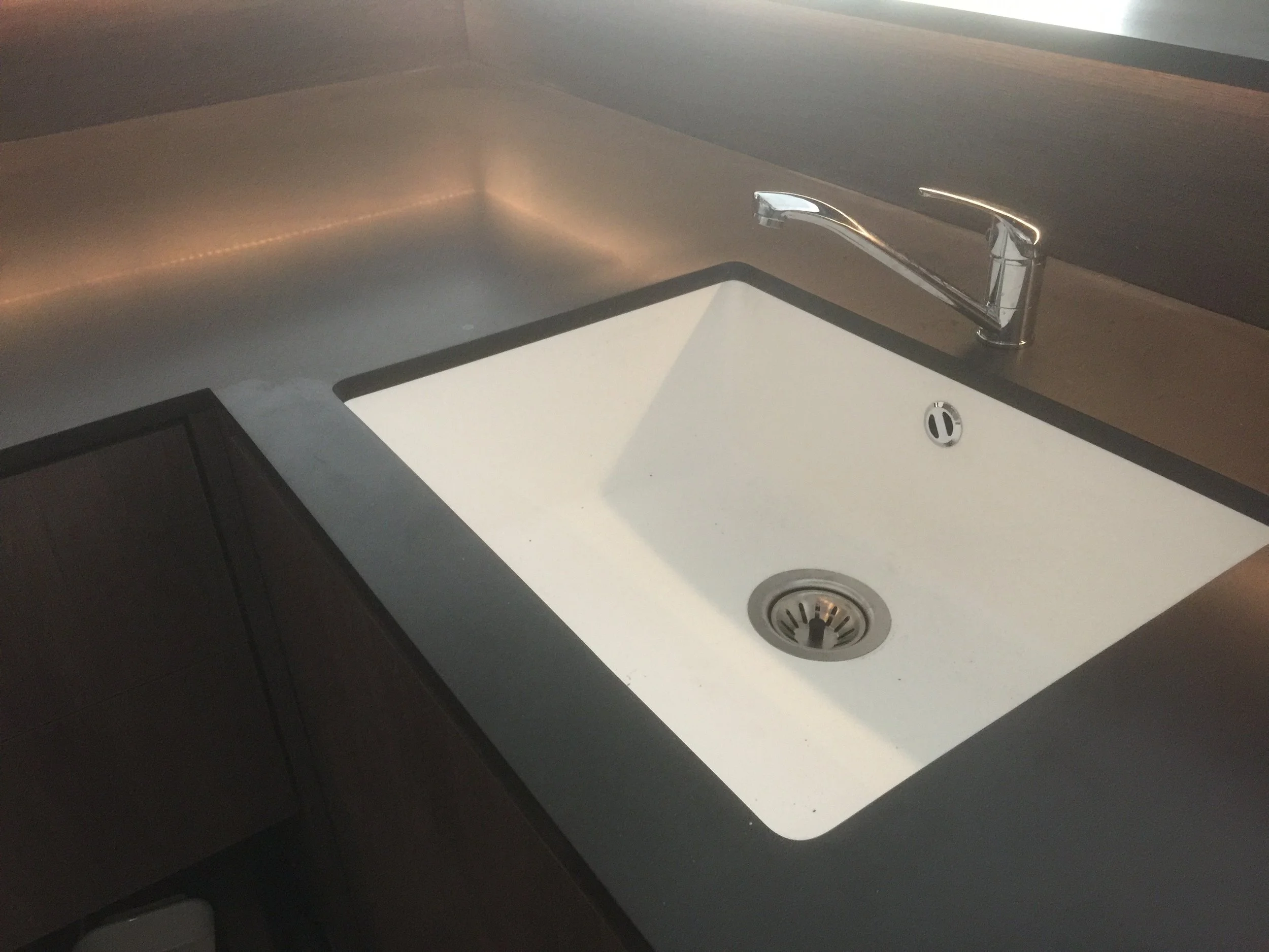 A kitchen sink with a chrome faucet, a white basin, and a round drain, alongside a dark countertop and cabinetry.