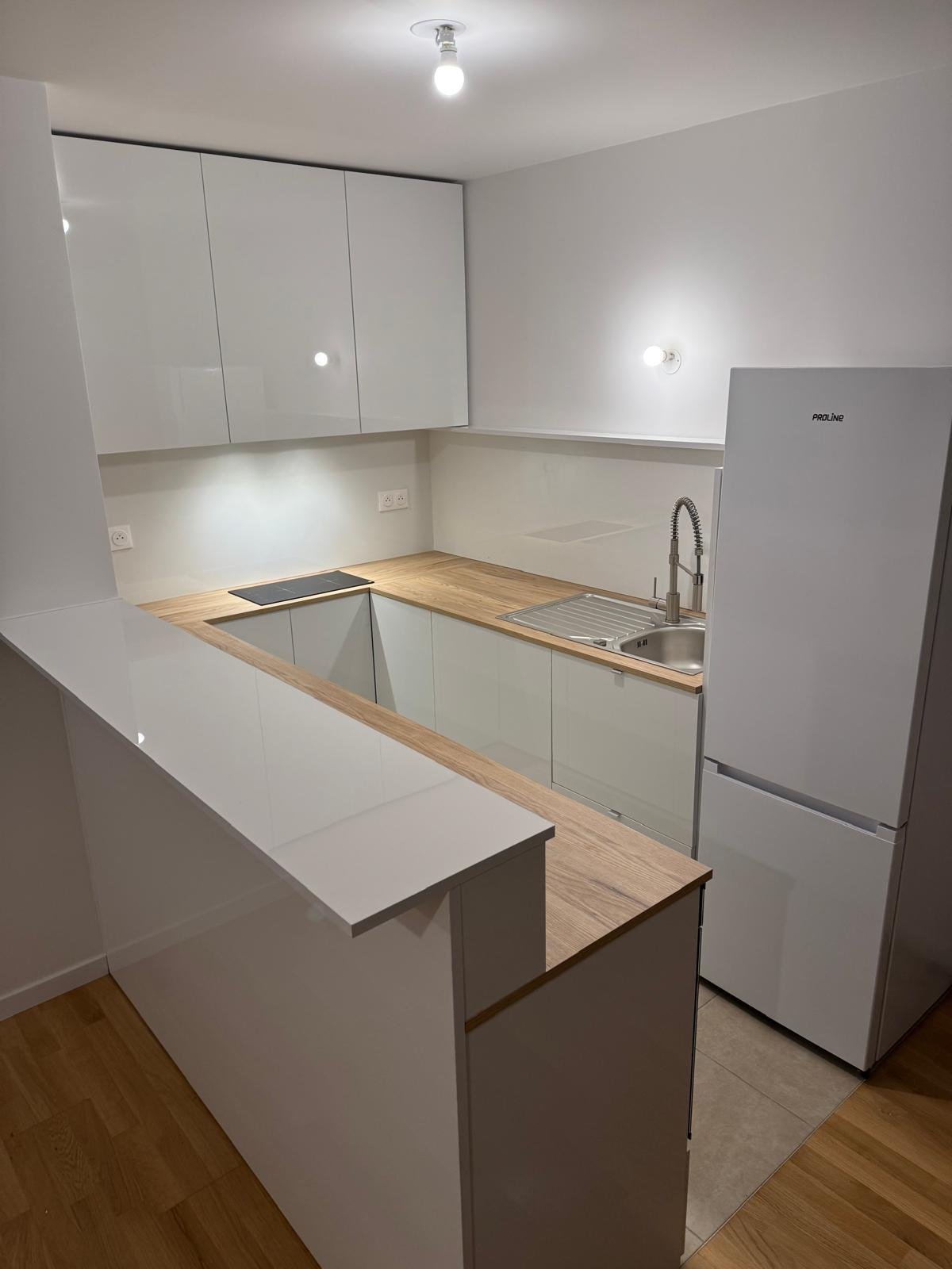Modern kitchen with white cabinets, wooden countertop, stainless steel sink, and a white refrigerator.