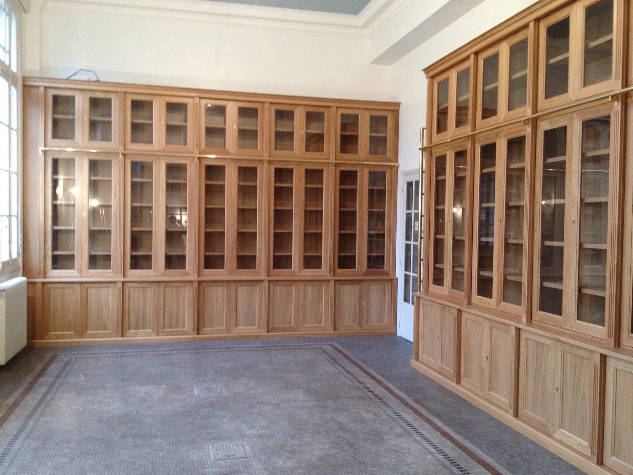 A spacious room with tall wooden bookshelves with glass doors and a patterned carpeted floor.