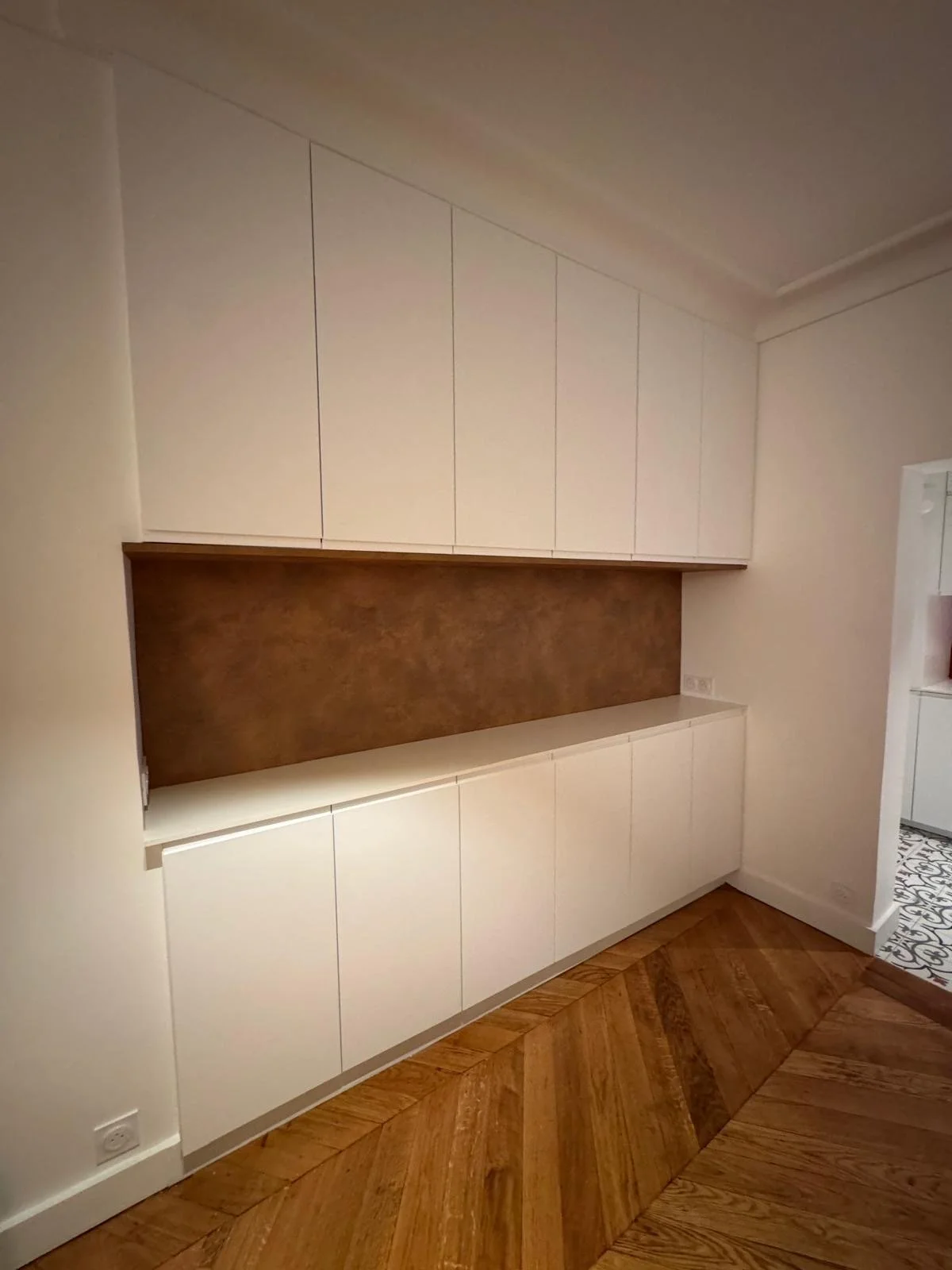 Modern built-in white storage cabinets with a brown wall panel in a room with parquet flooring.