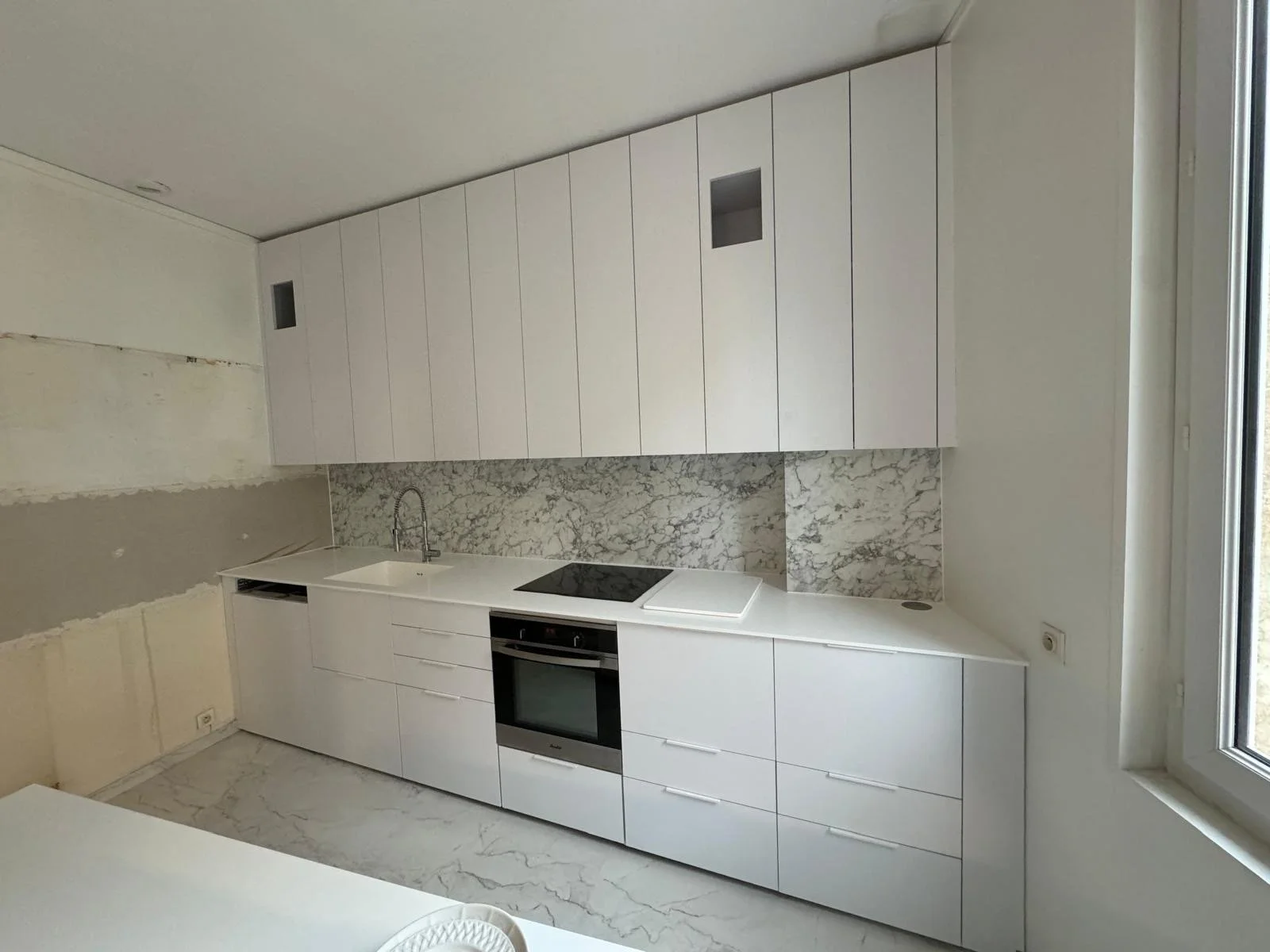 Modern kitchen with white cabinets, marble backsplash, and built-in oven