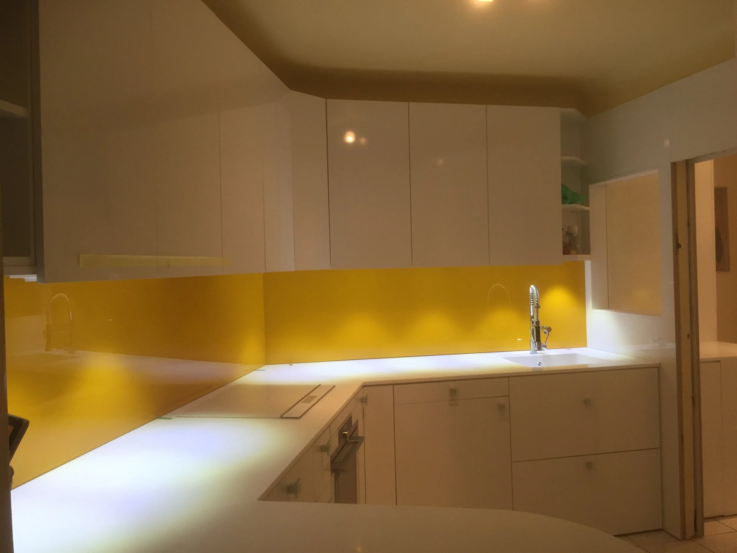 A modern kitchen with white cabinets, a yellow backsplash, a sink with a faucet, and a doorway leading to another room with yellow walls.