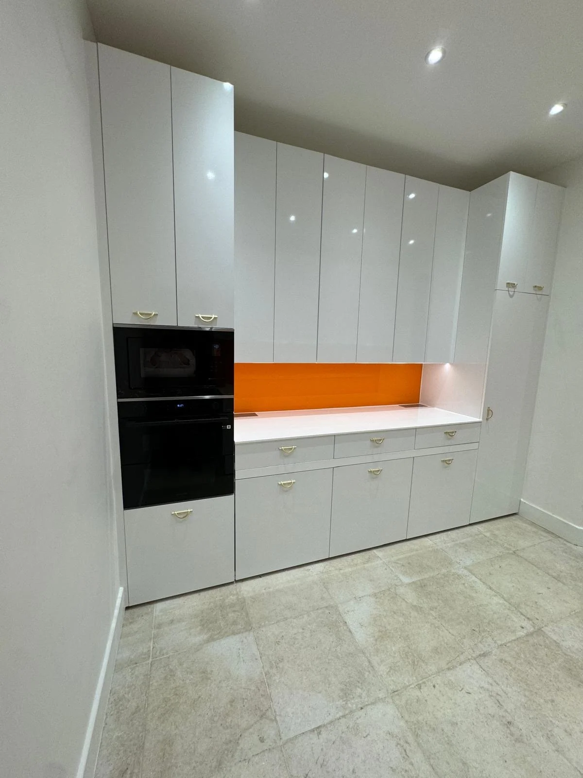 Modern kitchen with white cabinets, black oven and microwave, orange backsplash, and beige tiled floor.