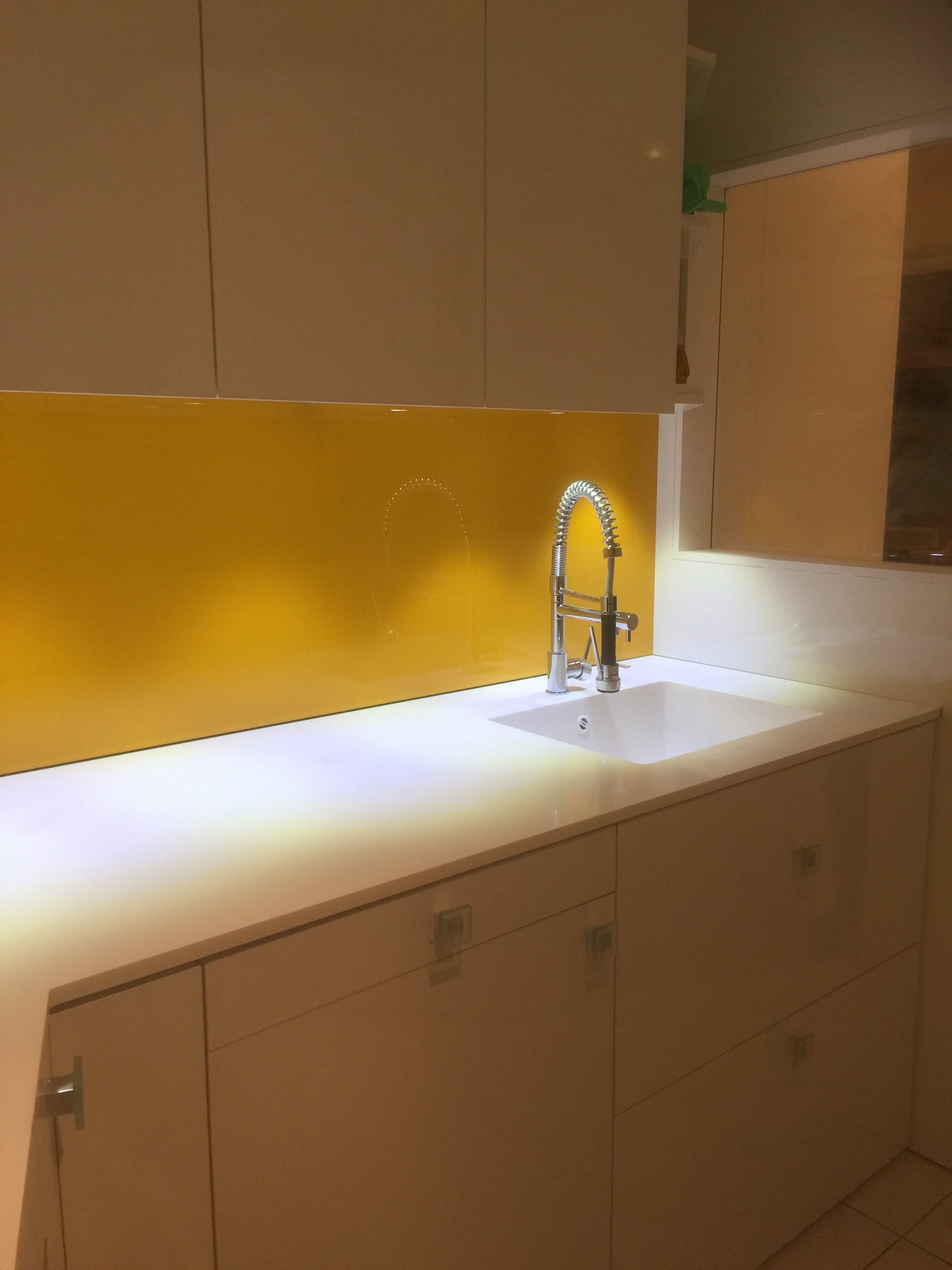 A modern kitchen with beige cabinets, a yellow backsplash, a white countertop, and a stainless steel faucet over a sink.