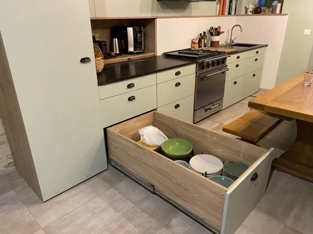 Kitchen with mint green cabinets, black countertop, oven, open shelf with kitchen items, and an open drawer with bowls and a tissue inside.