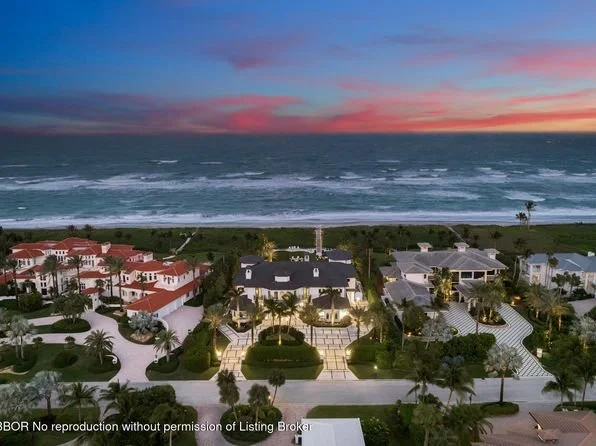 Aerial view of a beachfront neighborhood at sunset with houses, palm trees, and the ocean in the background.