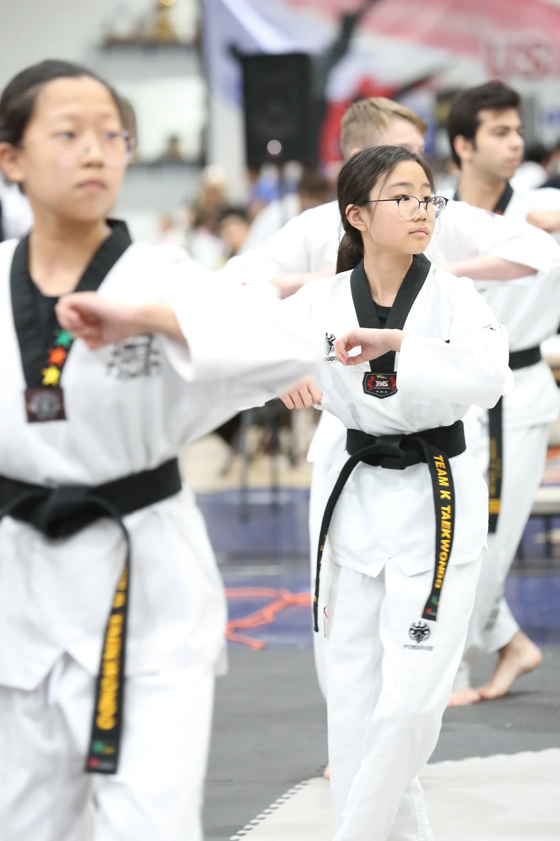 Children practicing martial arts in a dojo wearing traditional white uniforms with black belts, focusing and extending their arms.
