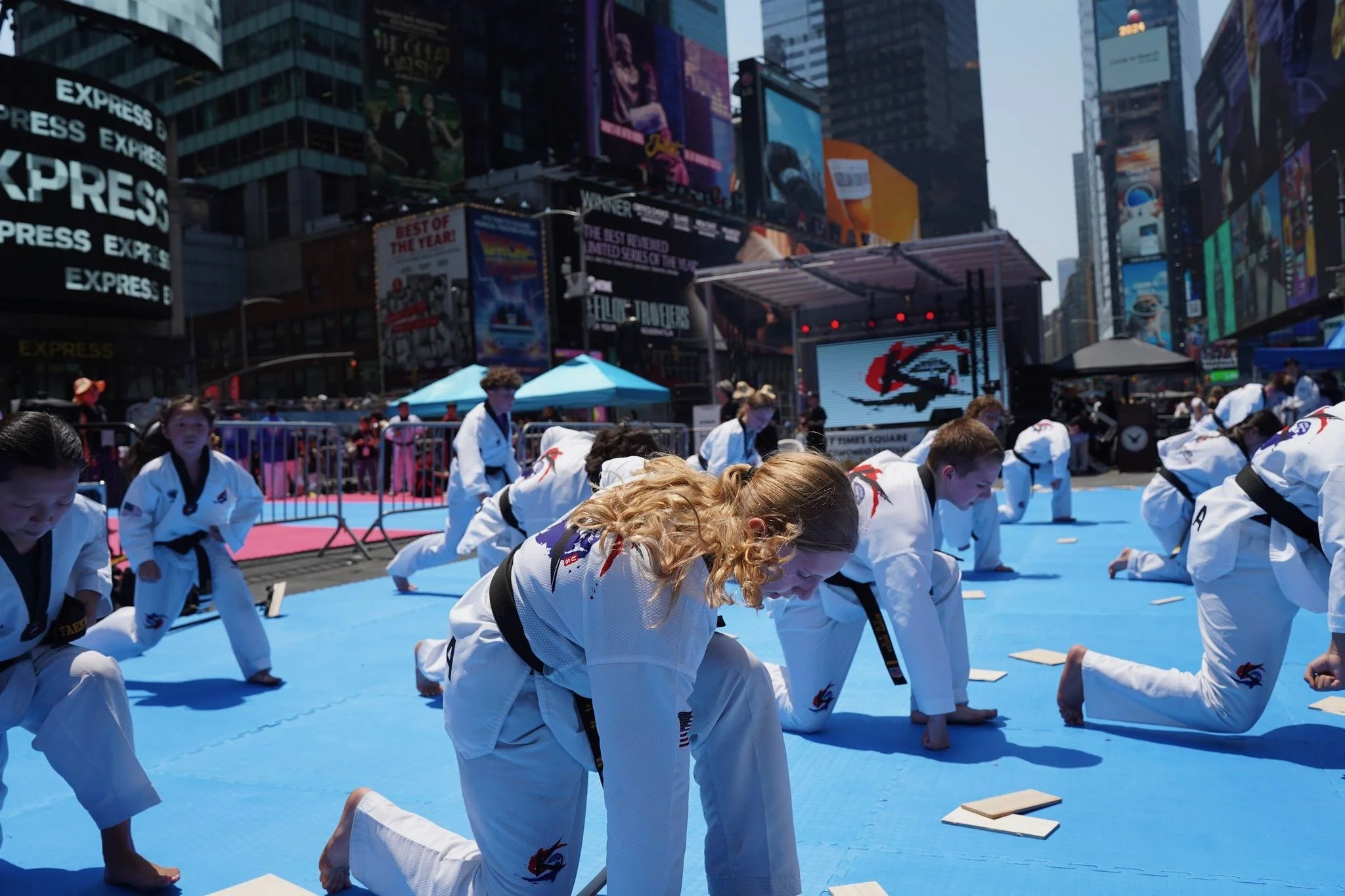 Group of martial artists practicing in Times Square with city billboards in the background.