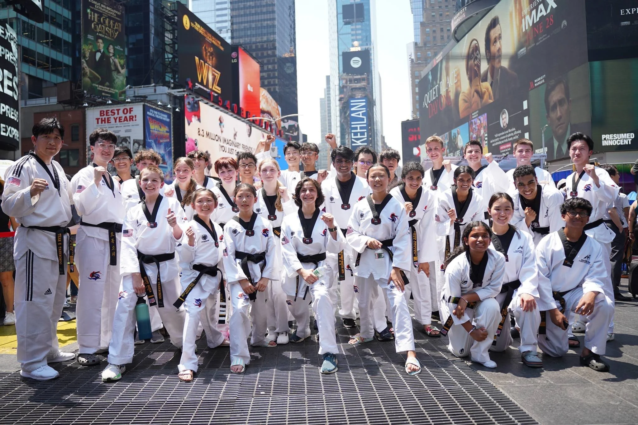Group of diverse children and teenagers in martial arts uniforms standing together in Times Square, New York City, celebrating after a martial arts event.