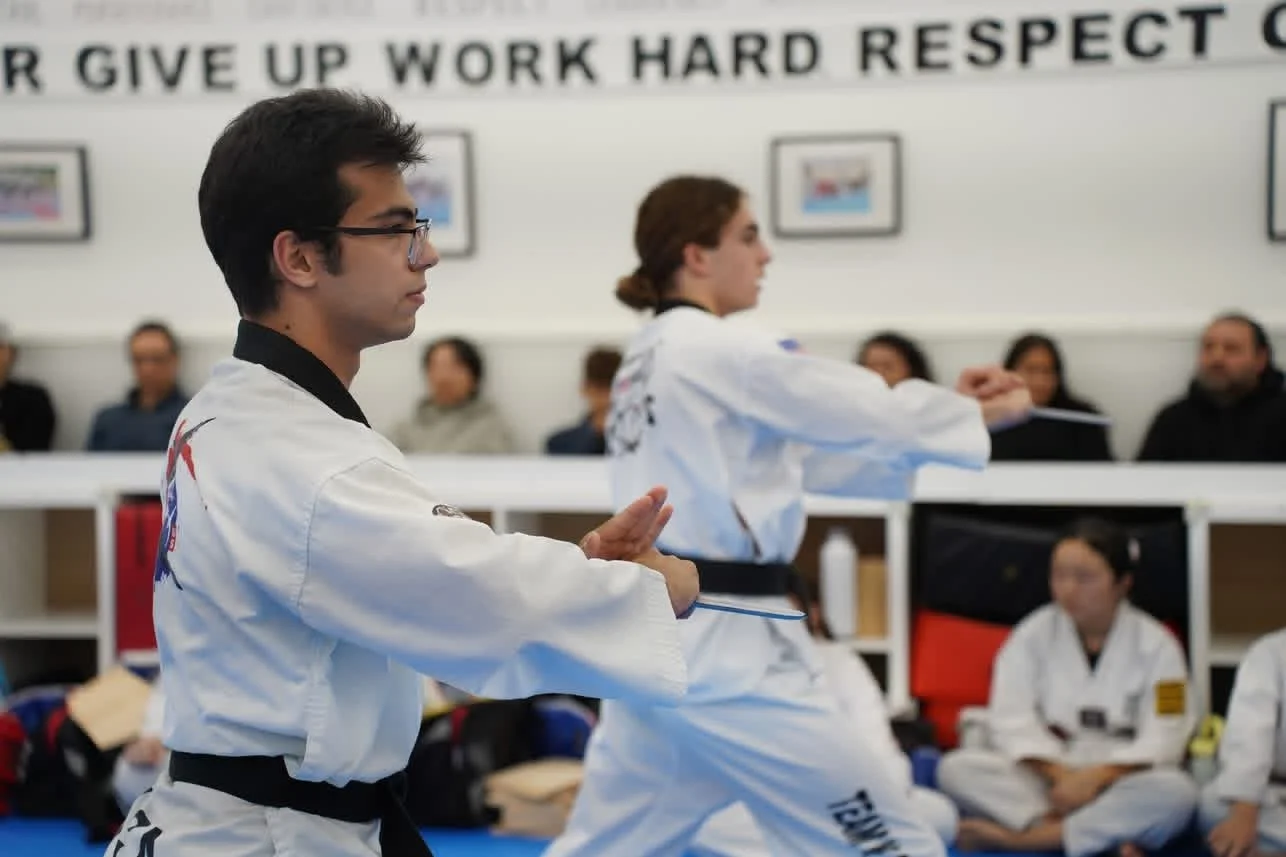 Two martial artists practicing in a dojo with spectators in the background