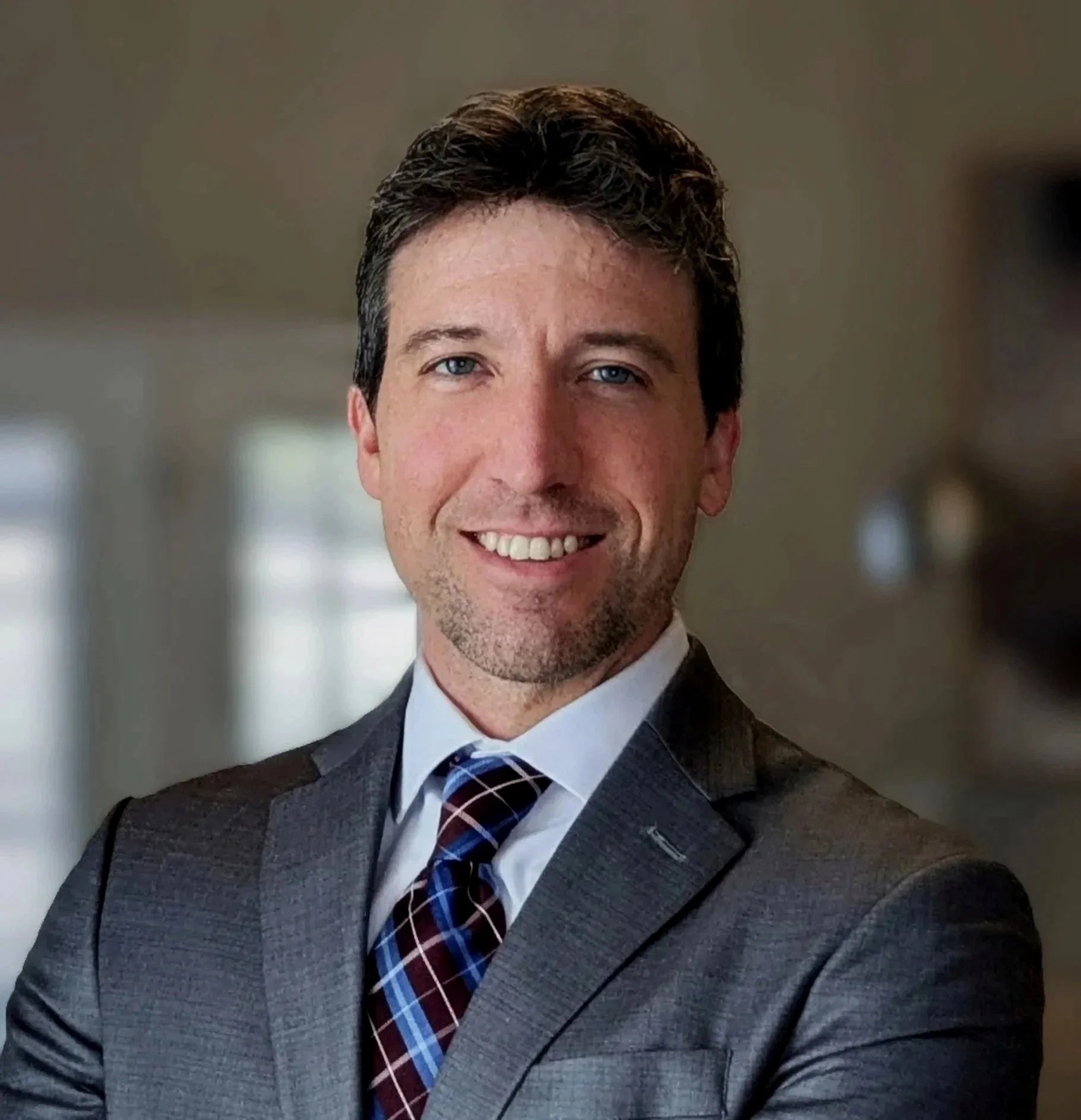 Headshot of a smiling man in a suit and tie, with a blurred background.