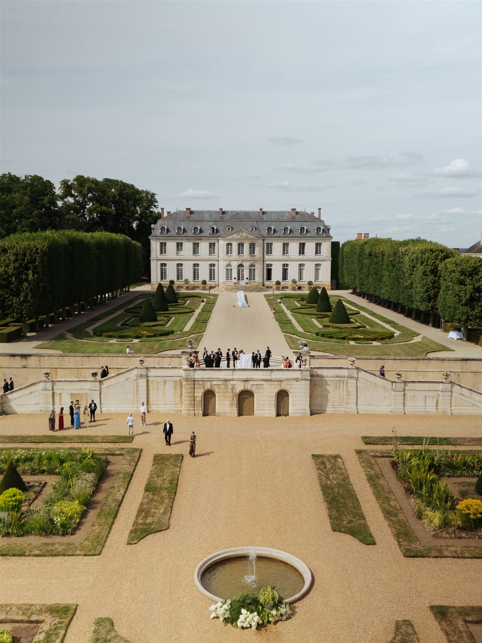Chateau Grand Luce with a formal garden and terrace, wedding guests gathered outside, and a fountain in the foreground.