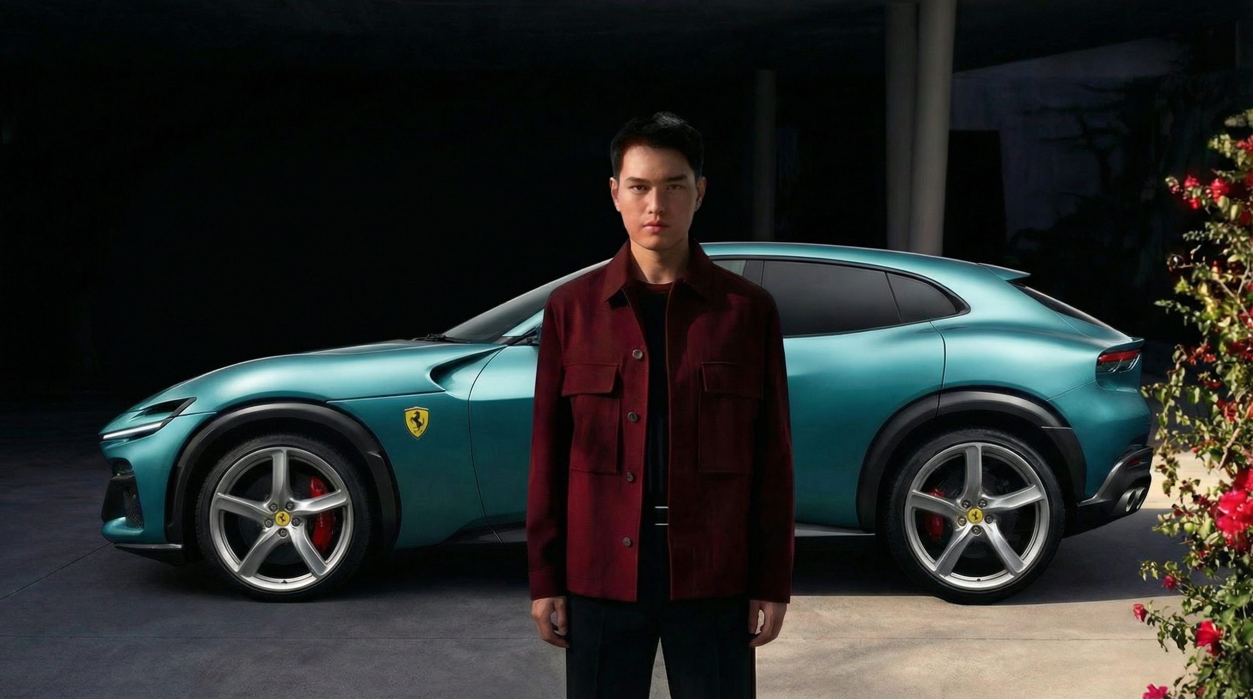 A young man standing in front of a teal Ferrari car at night.