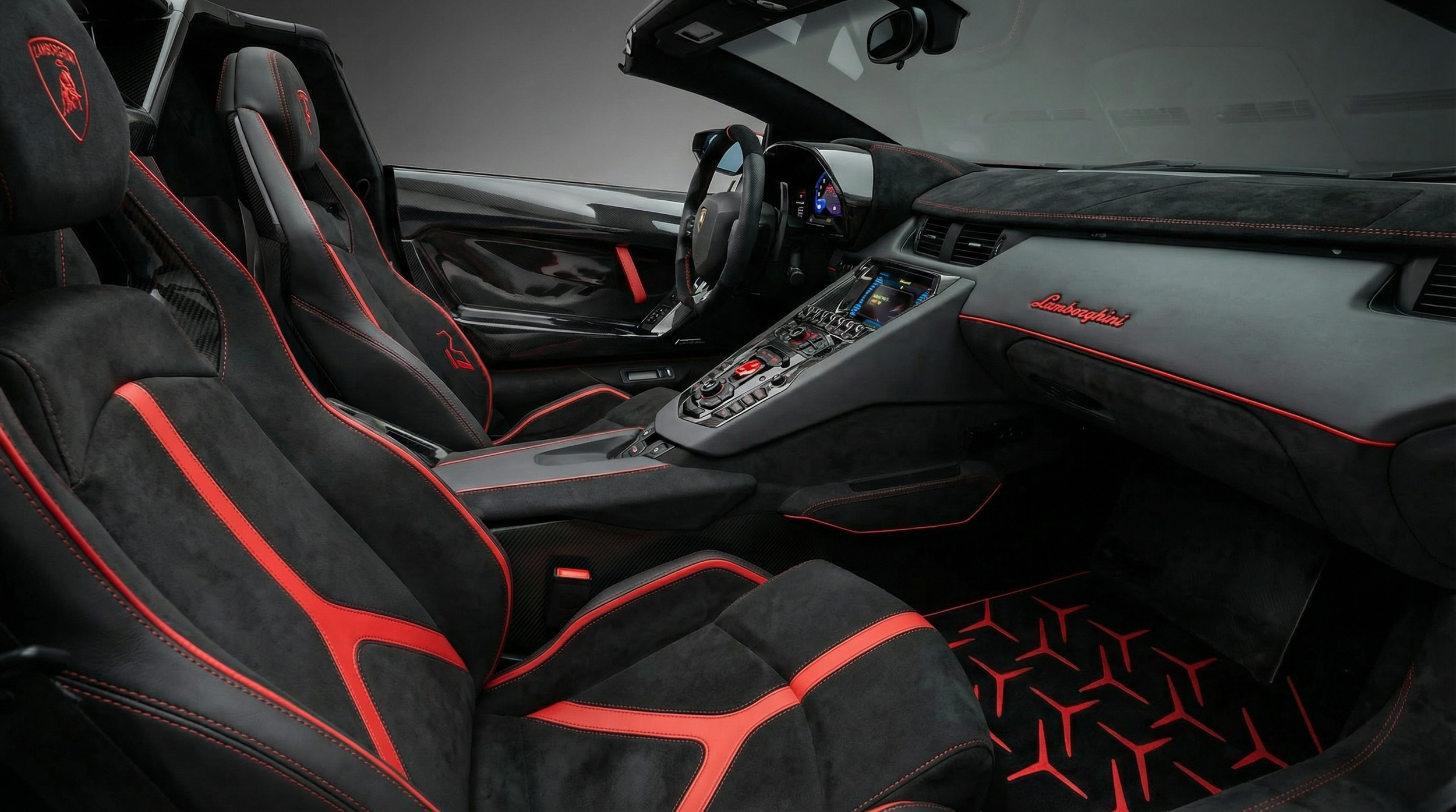 Interior of a black Lamborghini sports car with red accents, featuring racing-style bucket seats, a dashboard with digital displays, and a center console with control buttons.