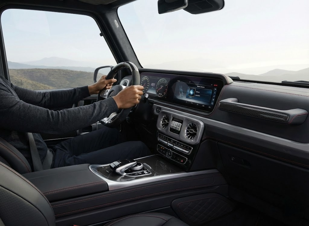 Interior of a vehicle showing a person driving on a mountainous road with digital dashboard display.