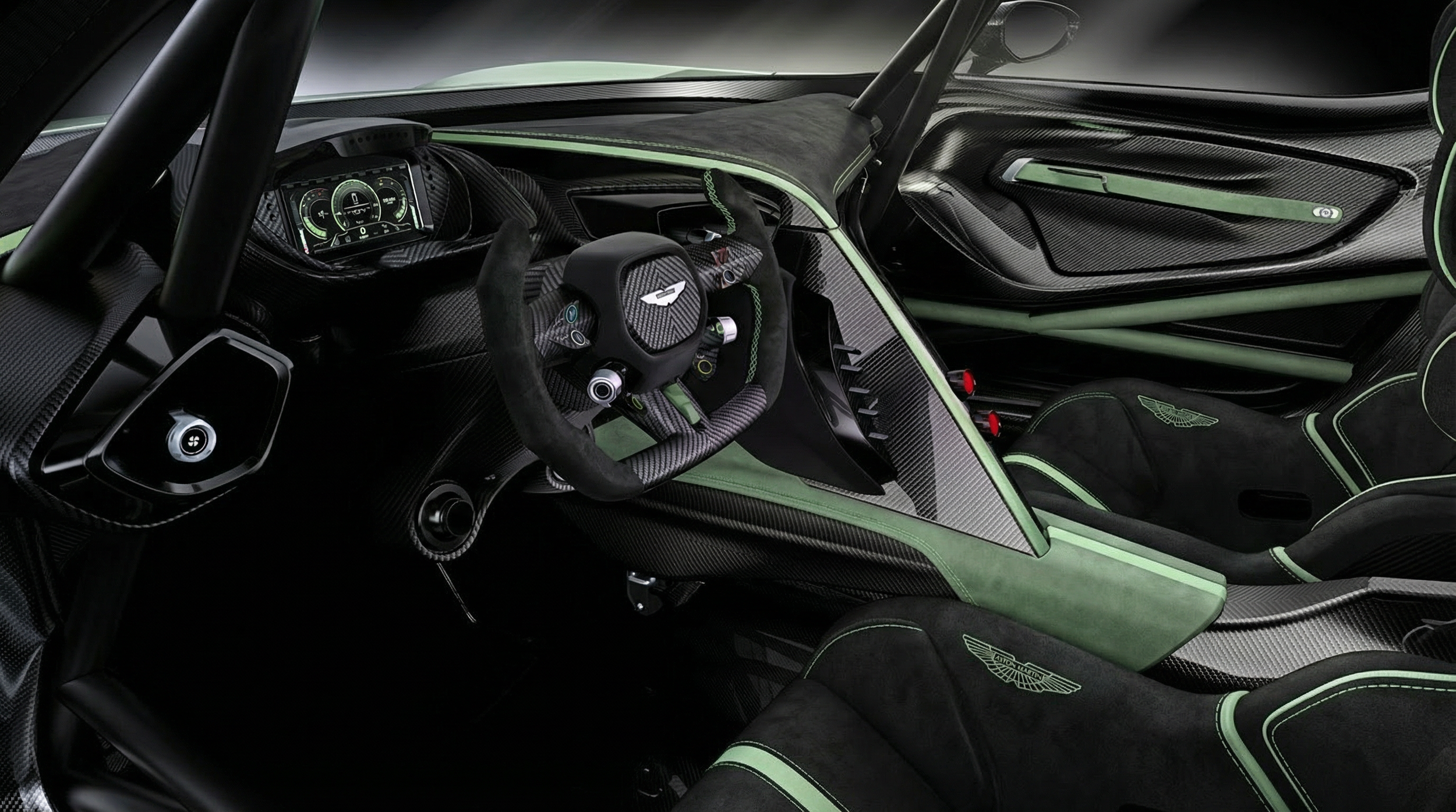 Interior of a high-performance race car with a carbon fiber steering wheel, digital dashboard, racing seats with green accents, and the Aston Martin logo.