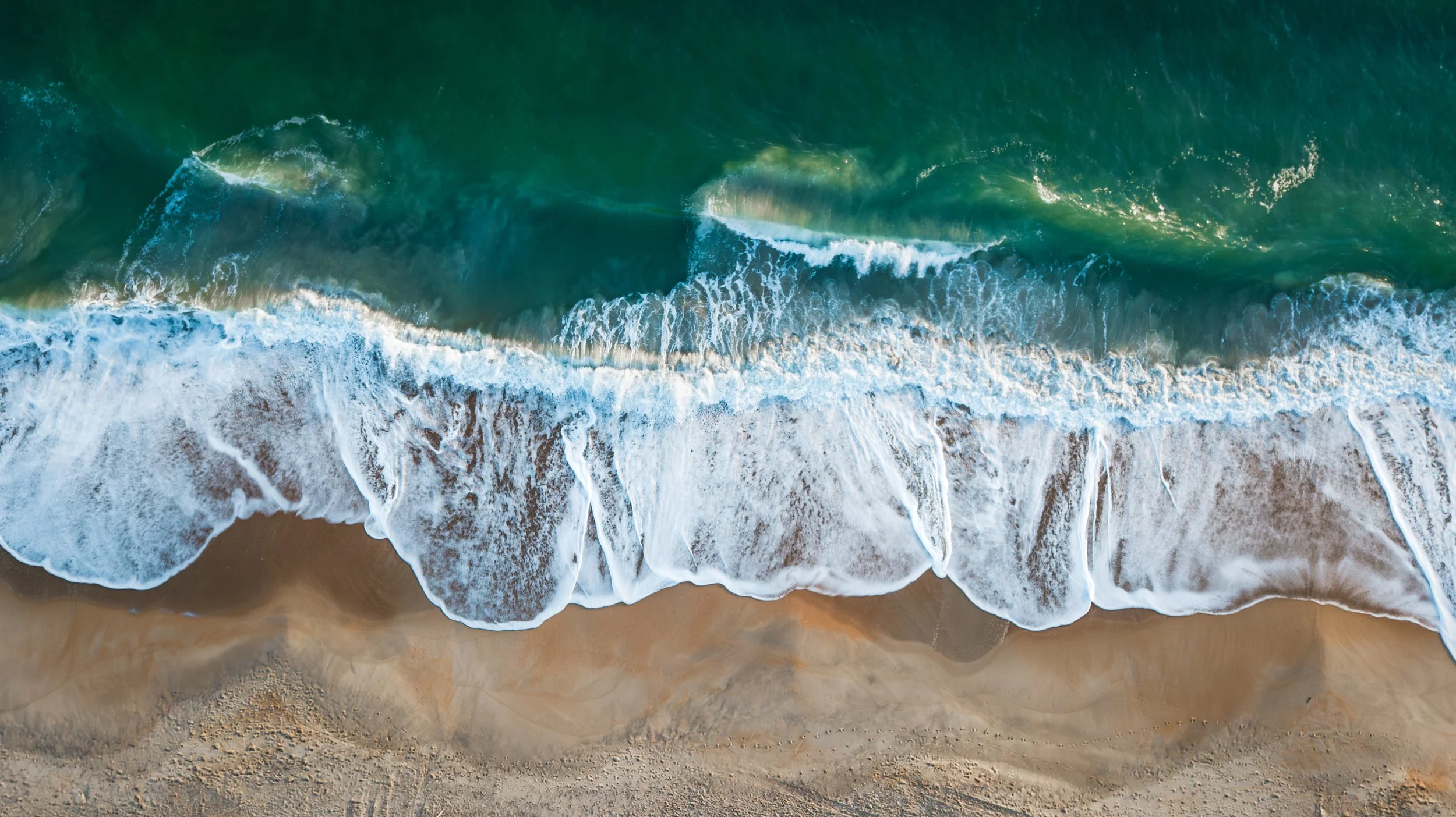 Aerial view of ocean waves crashing onto sandy beach.