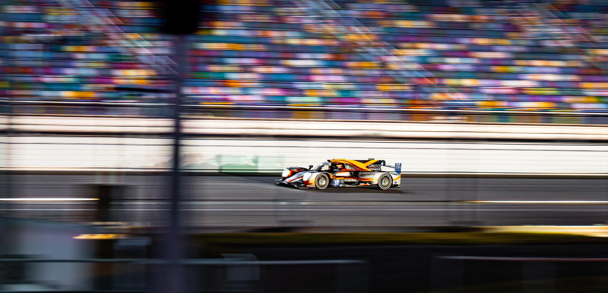 Race car speeding on a racetrack, blurred background of grandstand with colorful seats.